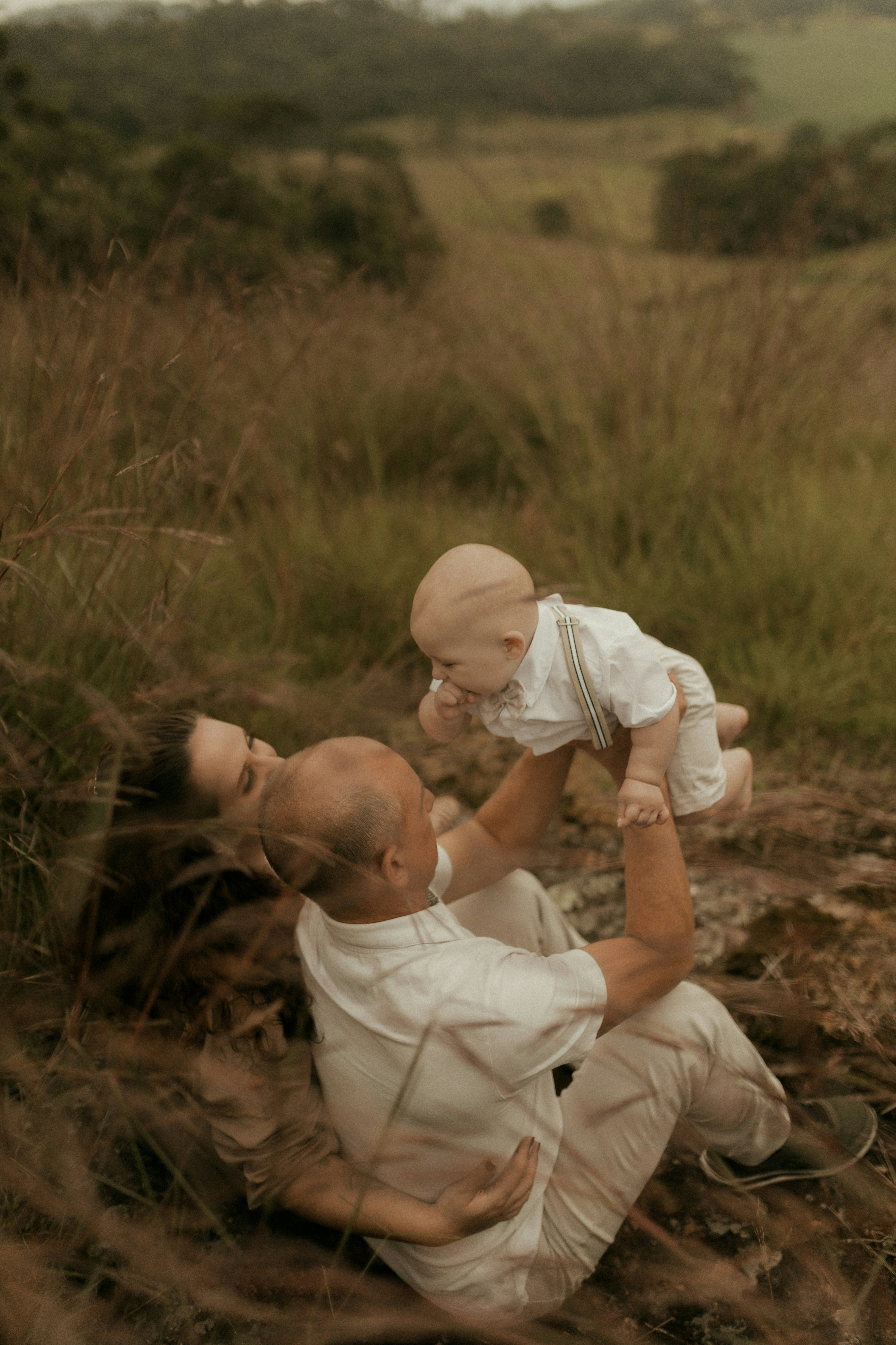 Ayah menggendong bayi di lapangan berumput bersama ibu