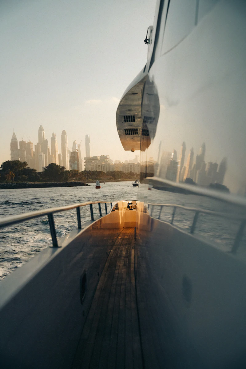 From the deck of a yacht at sunset, a city skyline glows across the water.