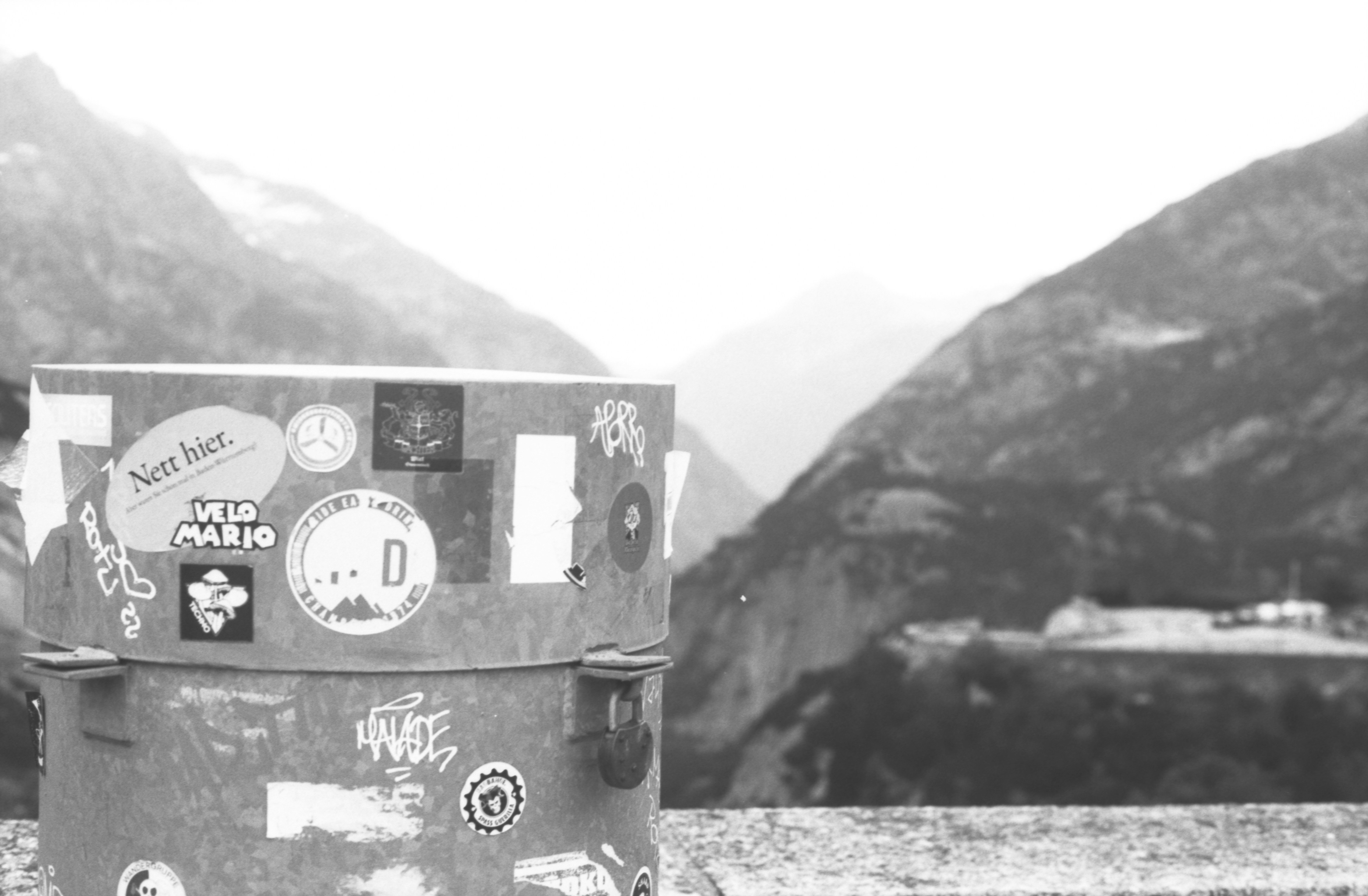 A cylindrical object covered in stickers with mountains behind.