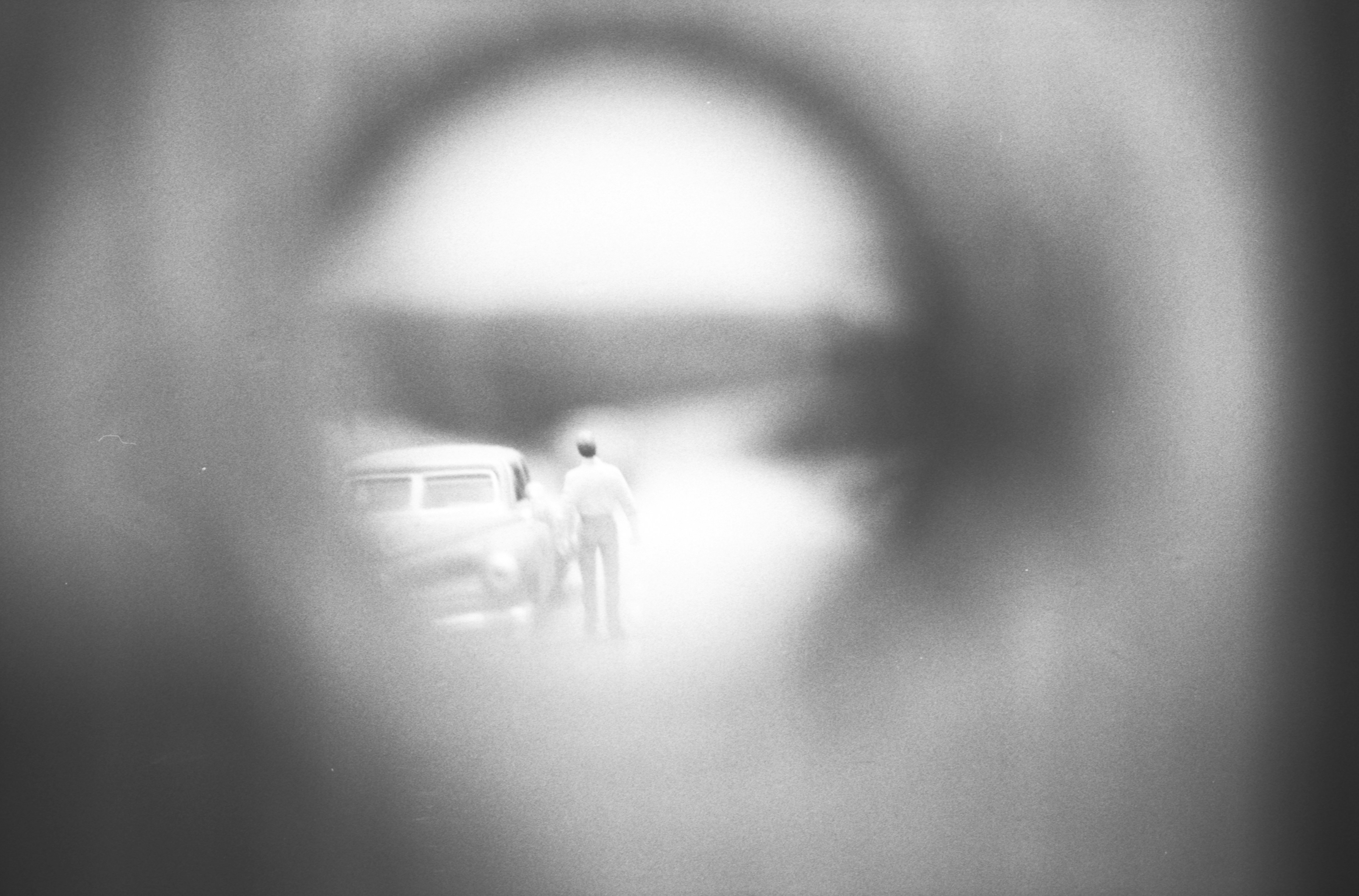 Two figures stand near a car, looking out.