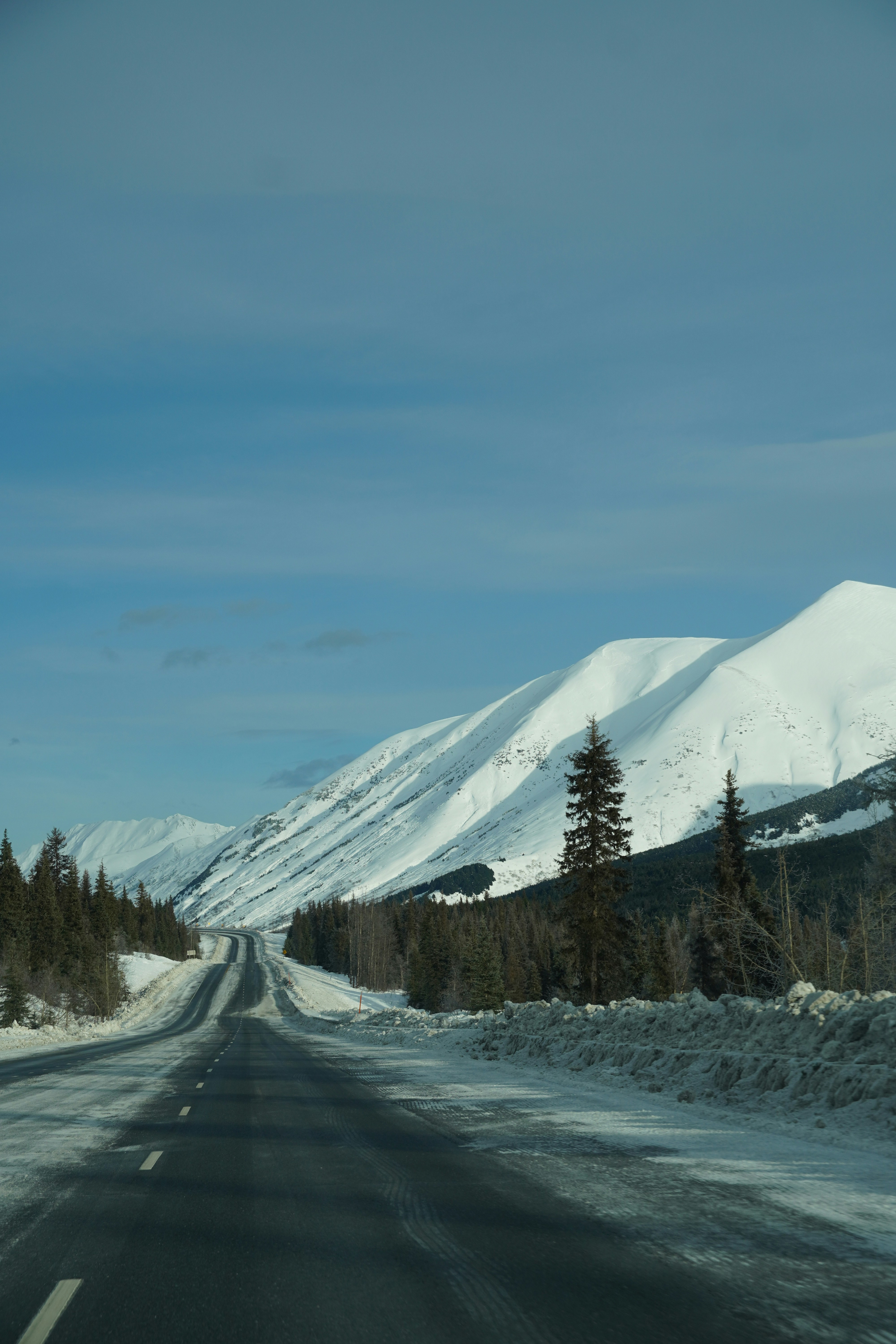 Snowy mountain road with evergreen trees under blue sky