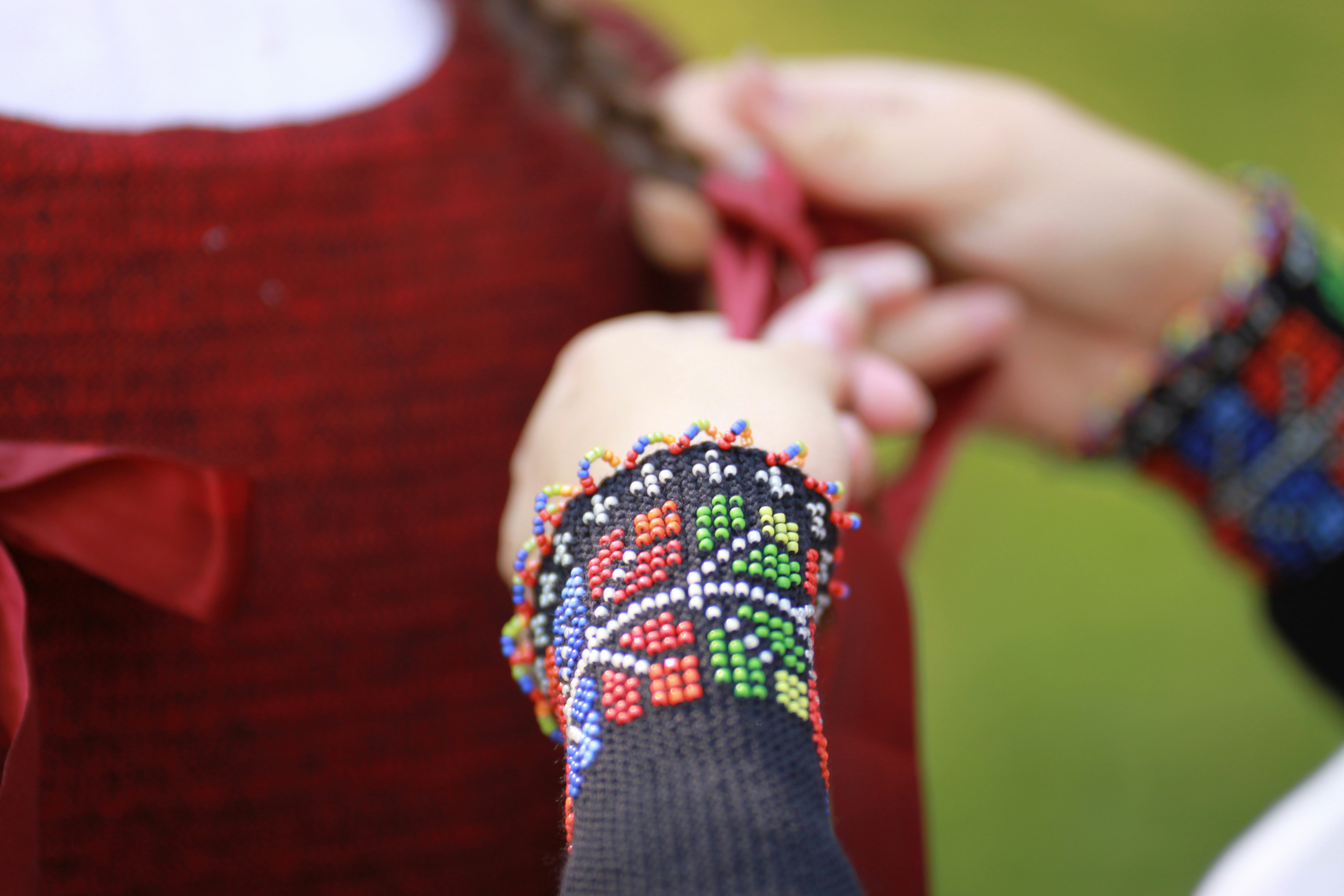 Mãos trançando o cabelo de uma jovem garota com pulseira de miçangas