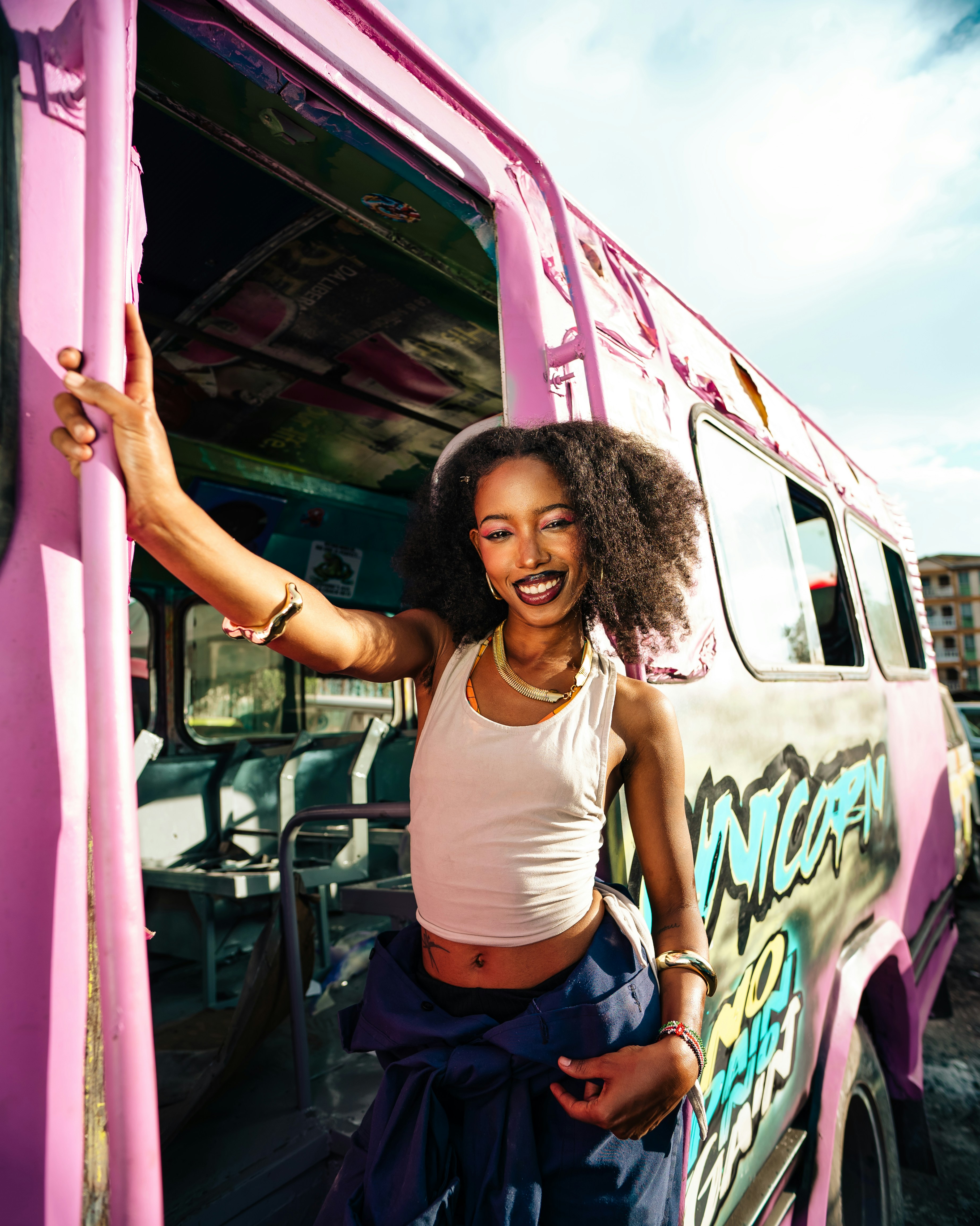 Eine lächelnde Frau steht an einem rosa Bus.