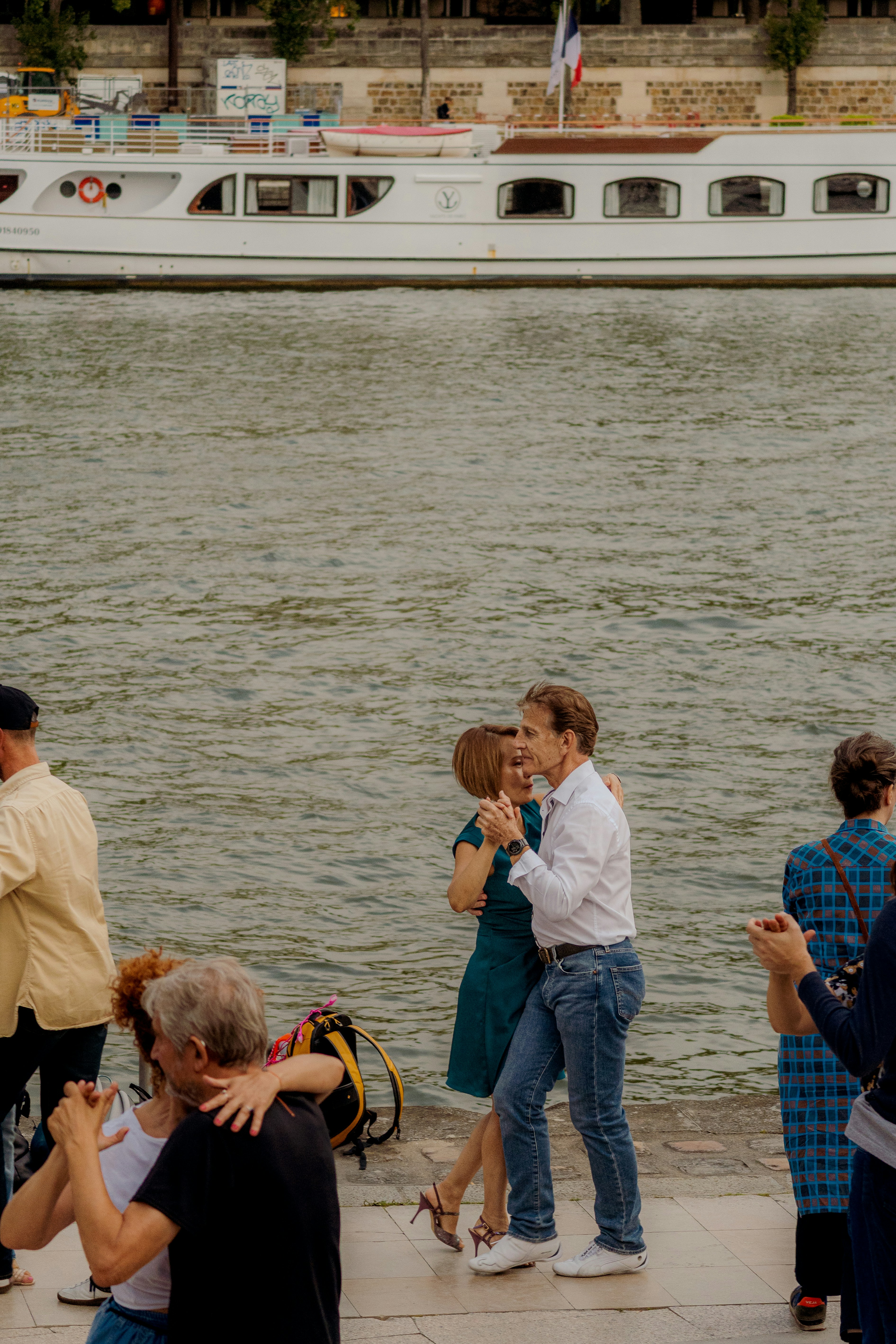 People dancing by the river with a boat in background