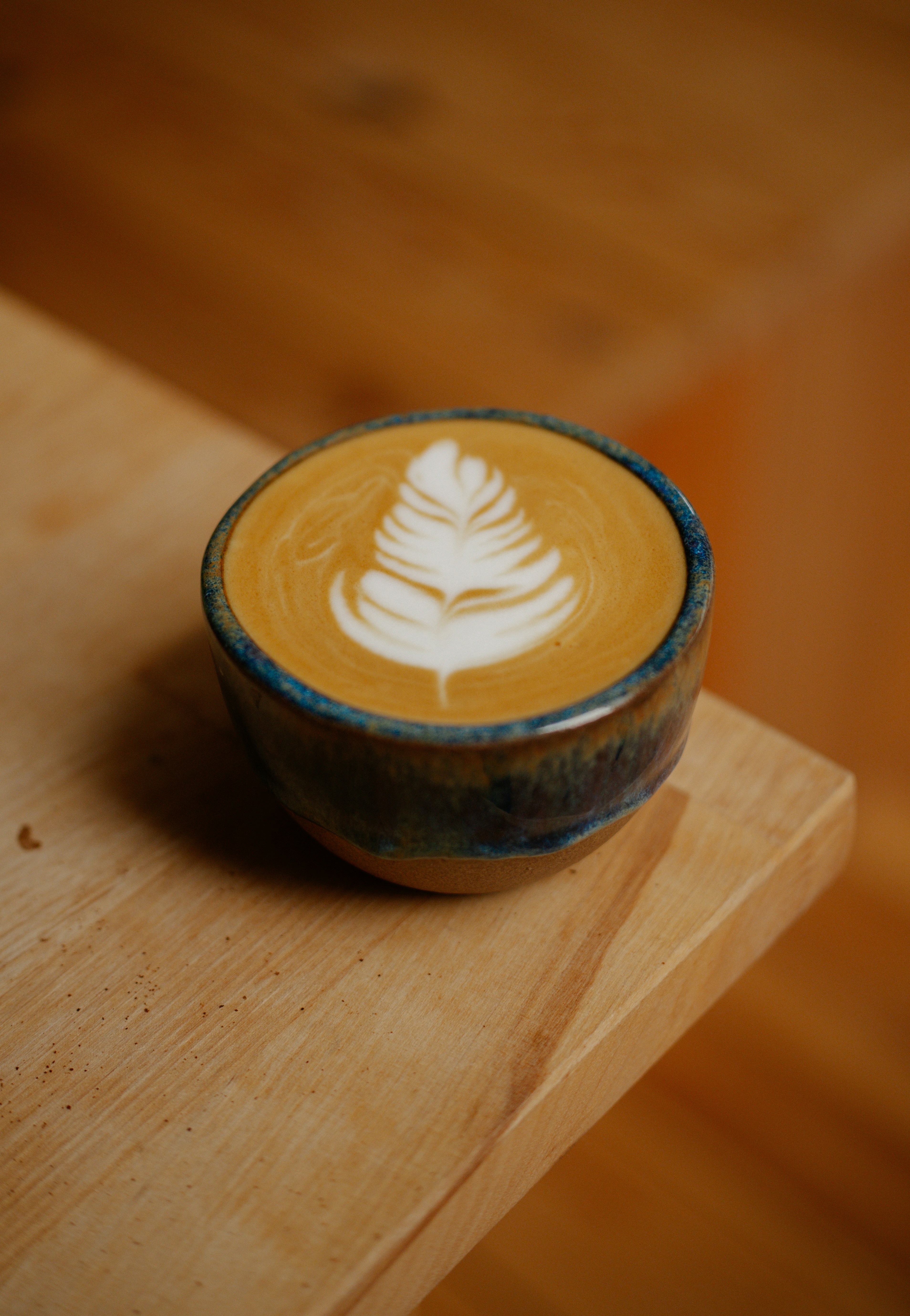 Latte art in a small ceramic cup on wooden surface