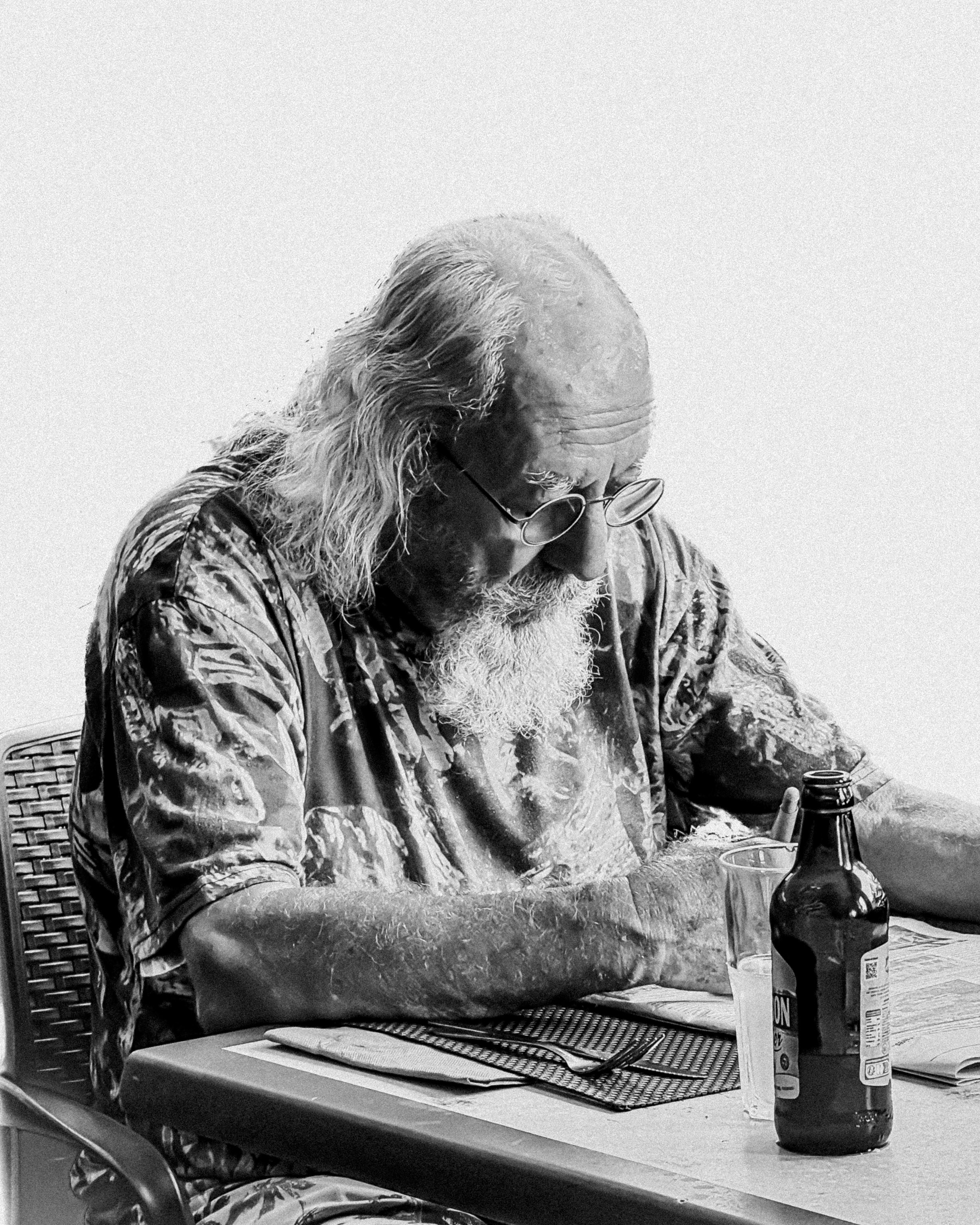 Elderly man with long hair and beard reading at table.