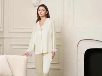 A woman in silk pajamas stands in a room.