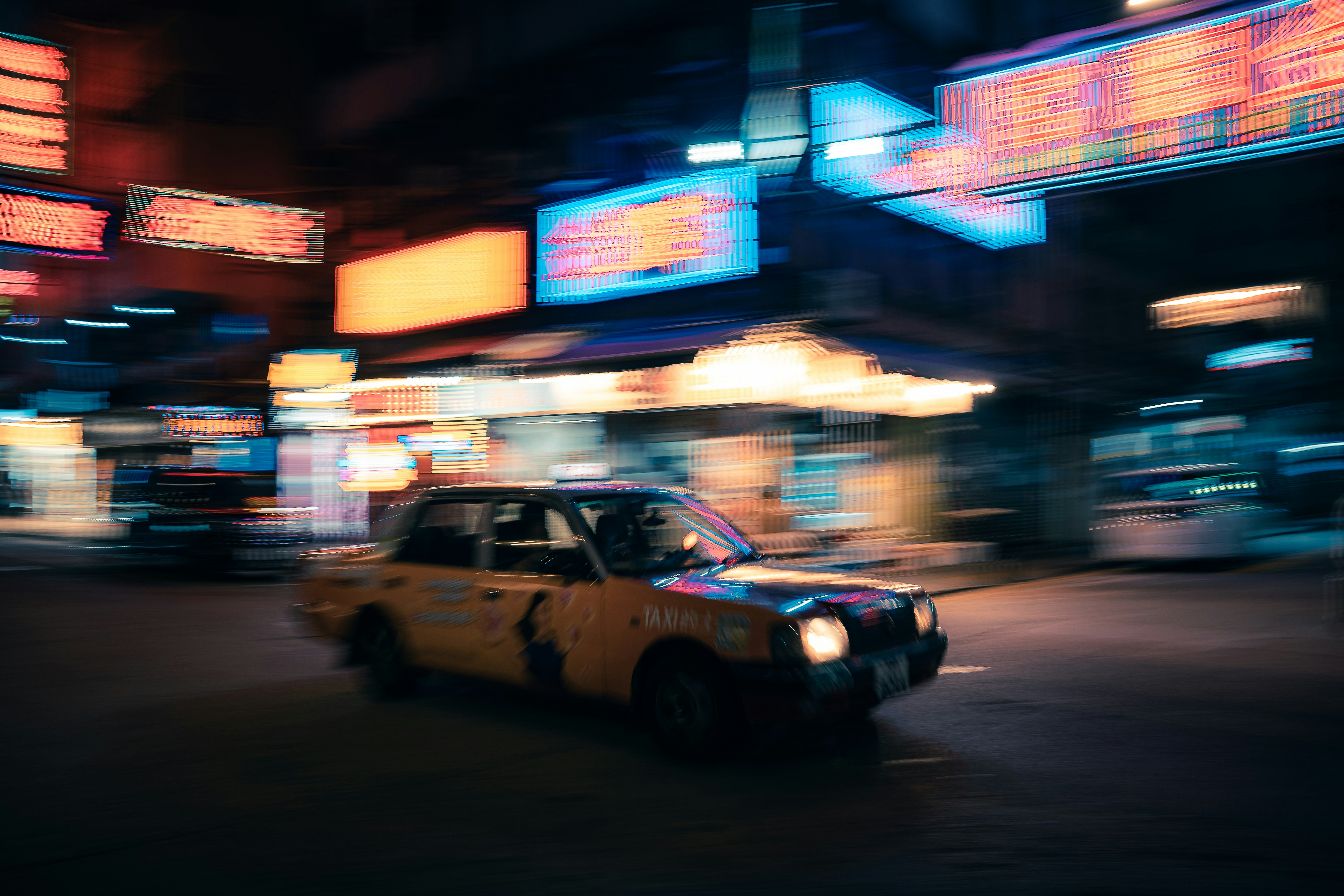 Yellow taxi drives through a neon-lit city street at night.
