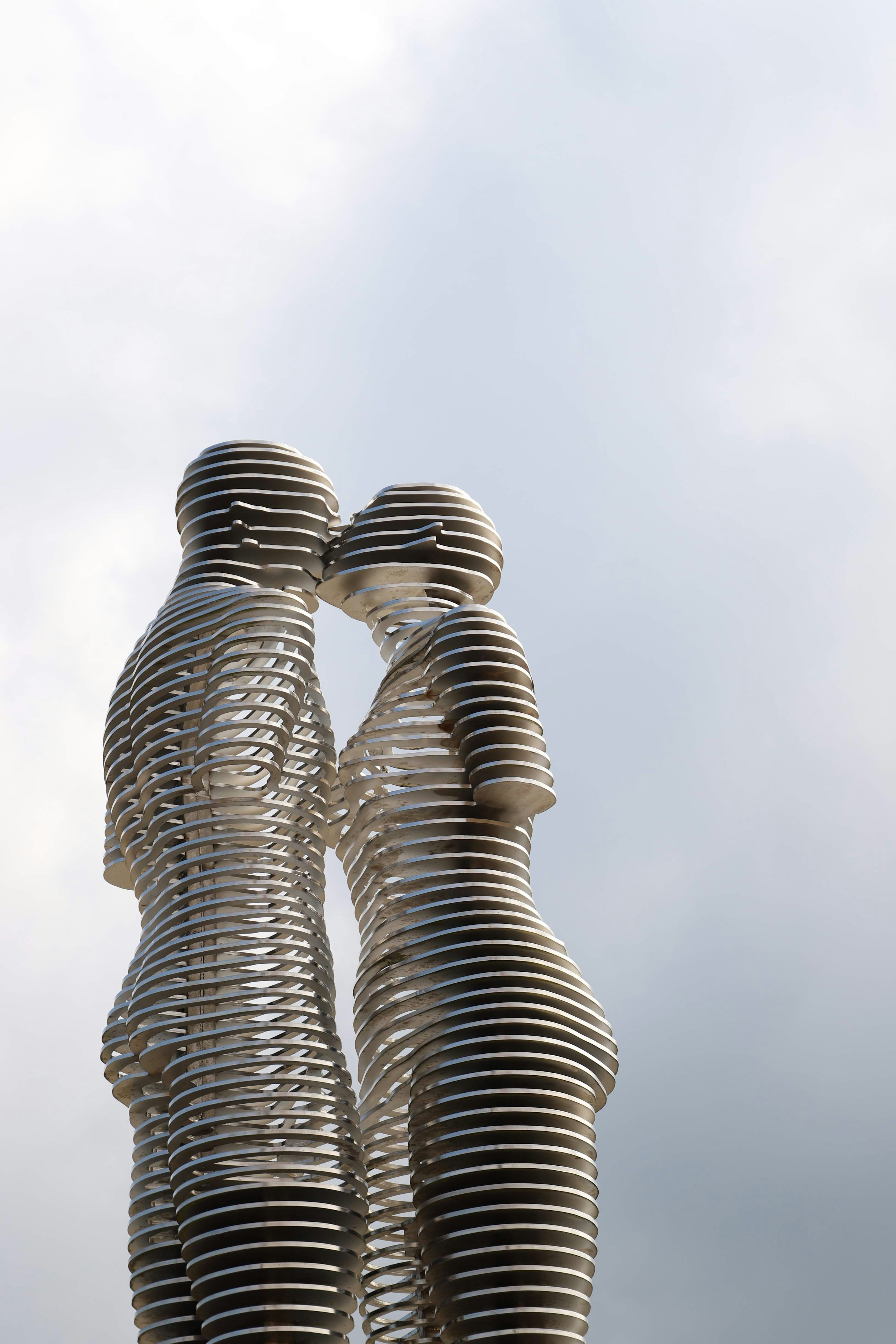 Two abstract metal figures kissing against a cloudy sky