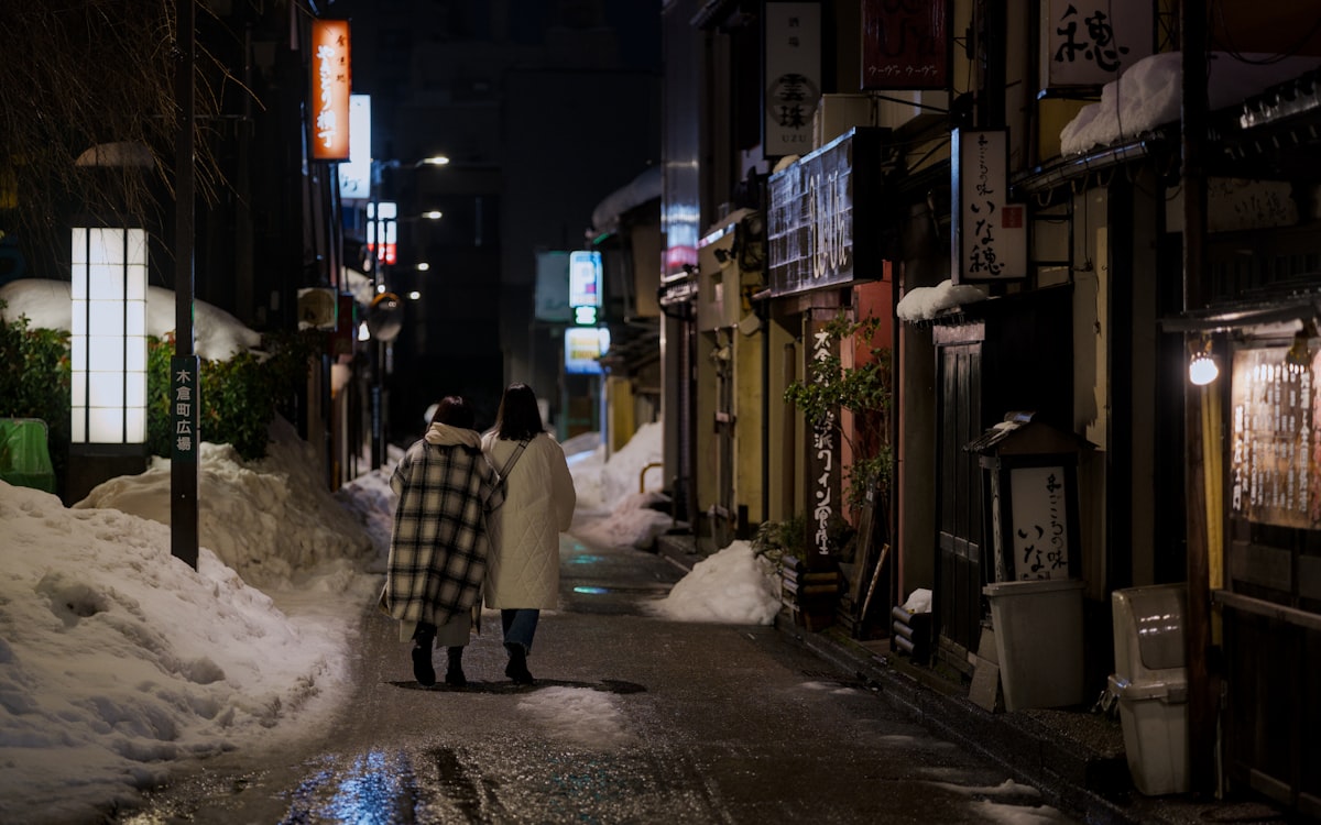 Kanazawa February — two people walking down a snow-covered street at night in the historic district