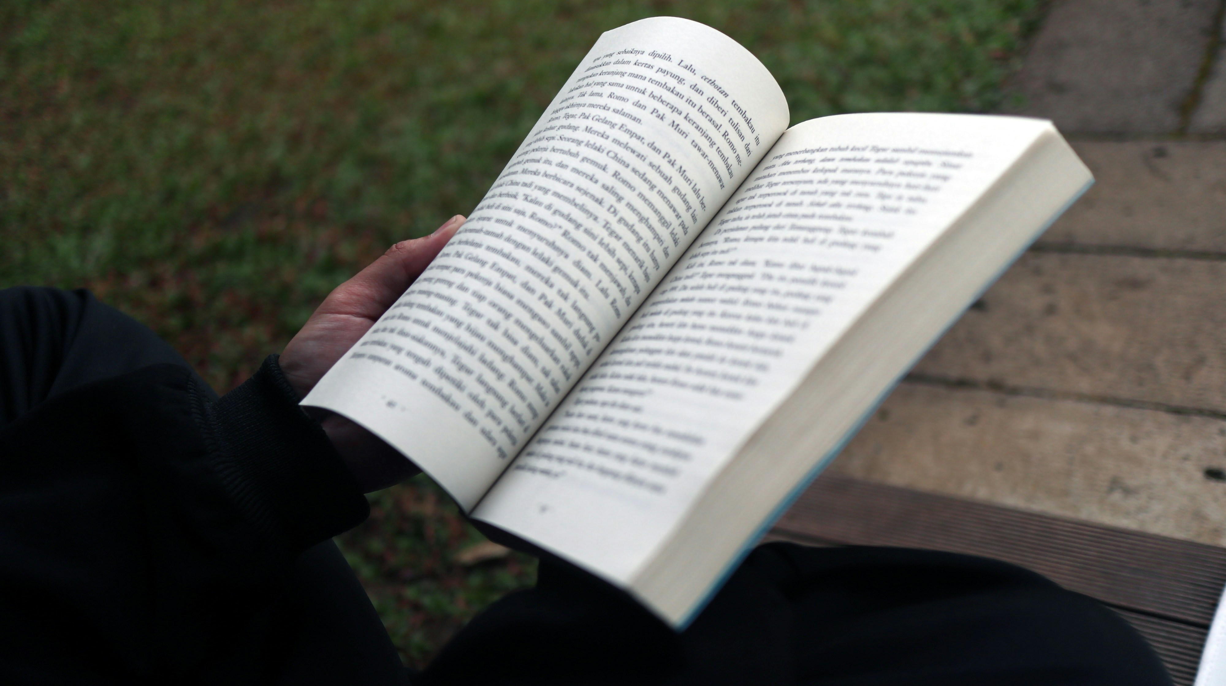 A person reading an open book outdoors