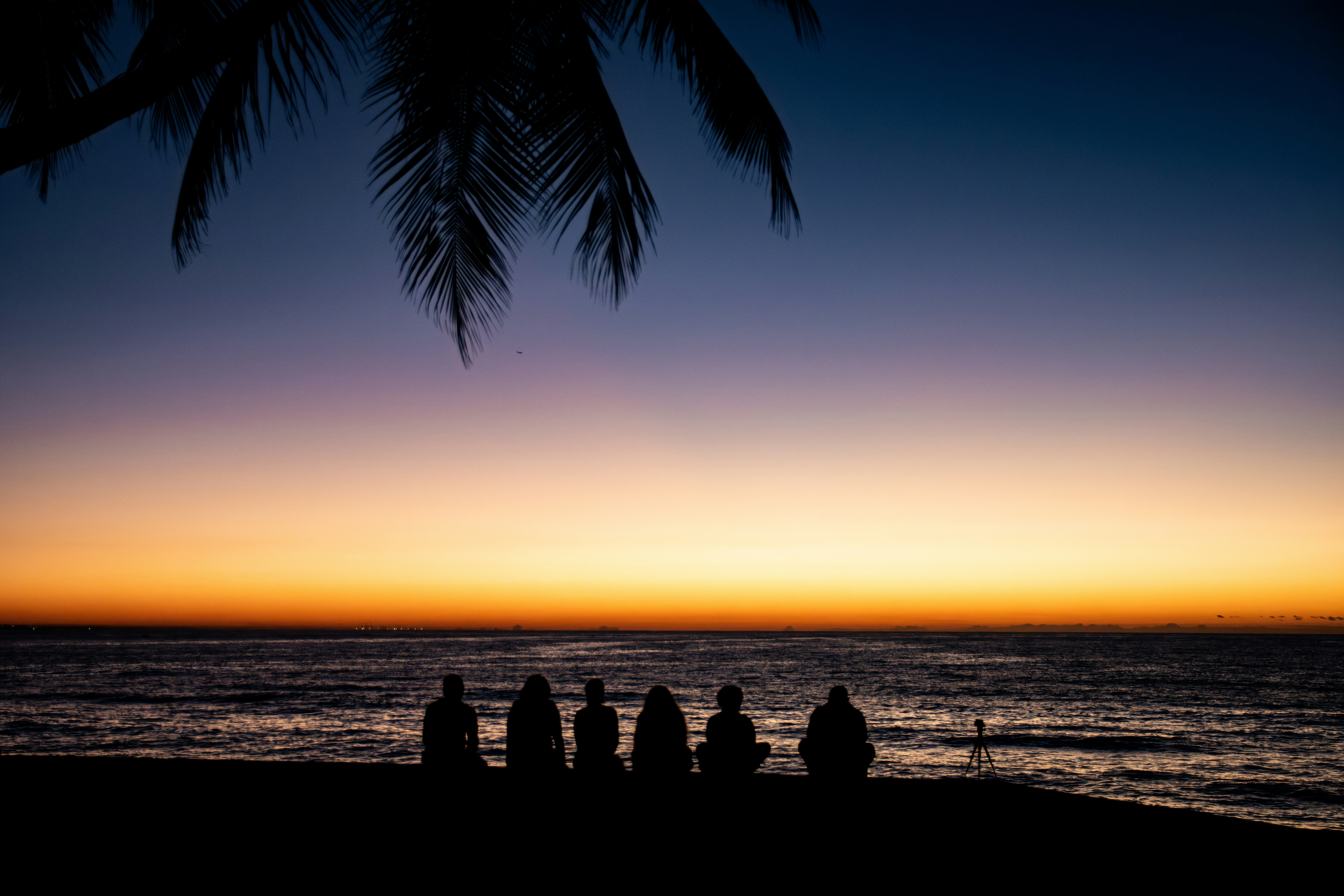 Silhuetas de personas observando una vibrante puesta de sol sobre el océano.