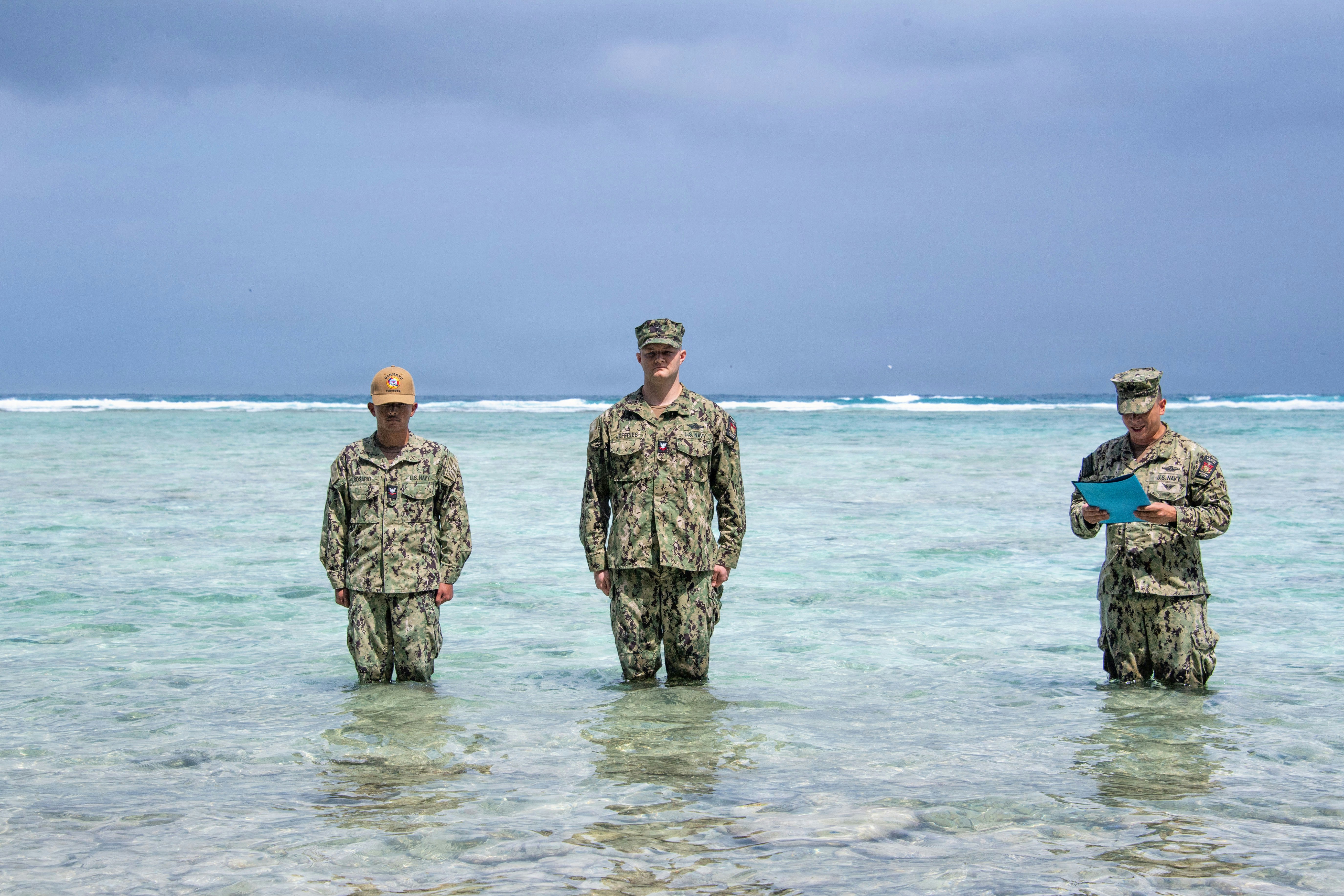 Tres personas con uniforme de pie en aguas poco profundas del océano.