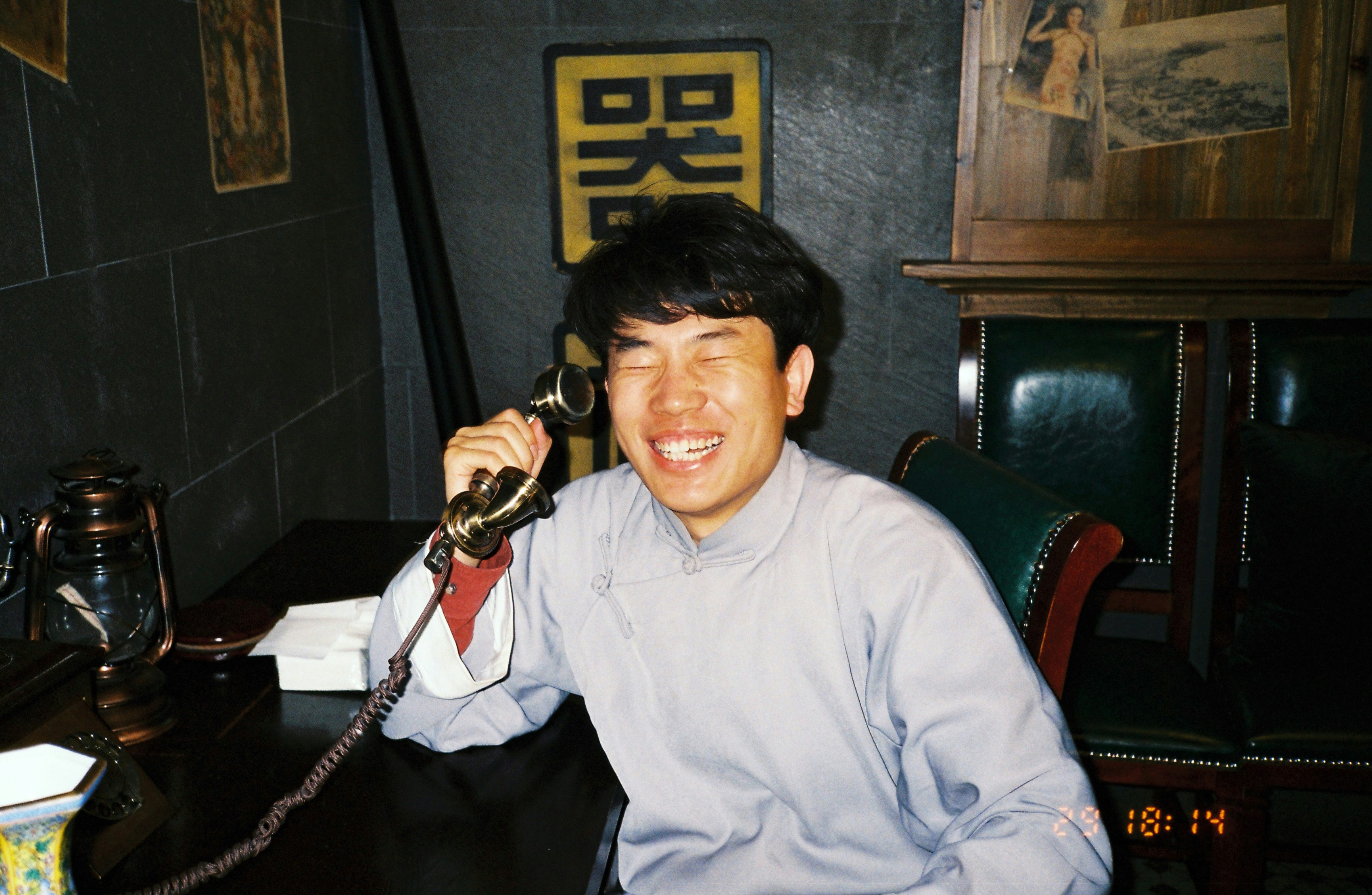 A man laughs while talking on an old telephone.