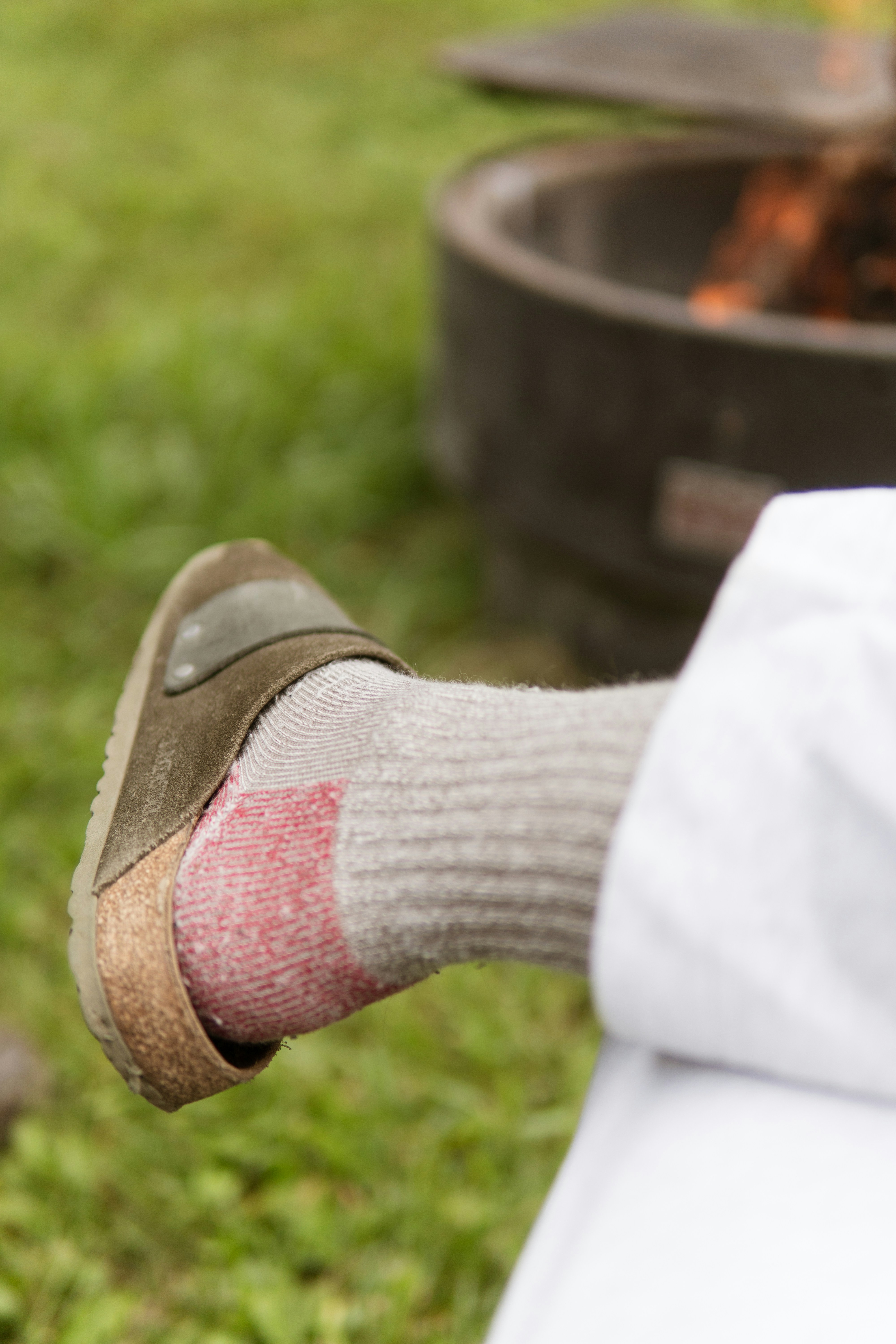 Person's foot in sock and sandal near campfire