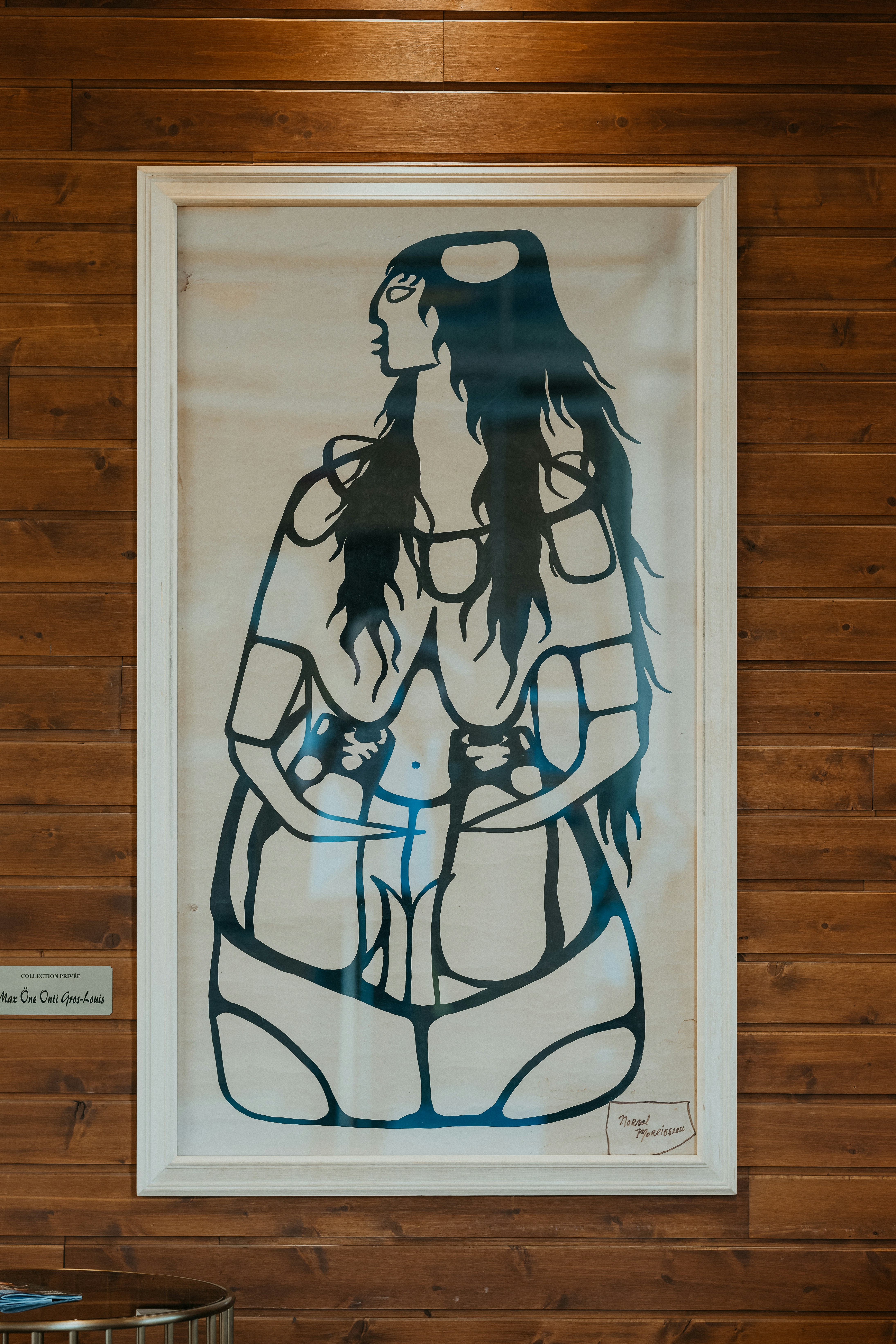 Gerahmtes Kunstwerk einer stilisierten Figur an einer Holzwand