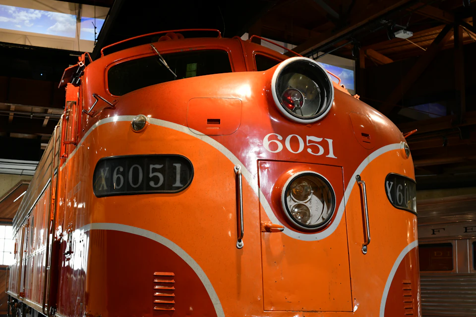 Orange and white train engine 6051 faces left in a large industrial warehouse interior