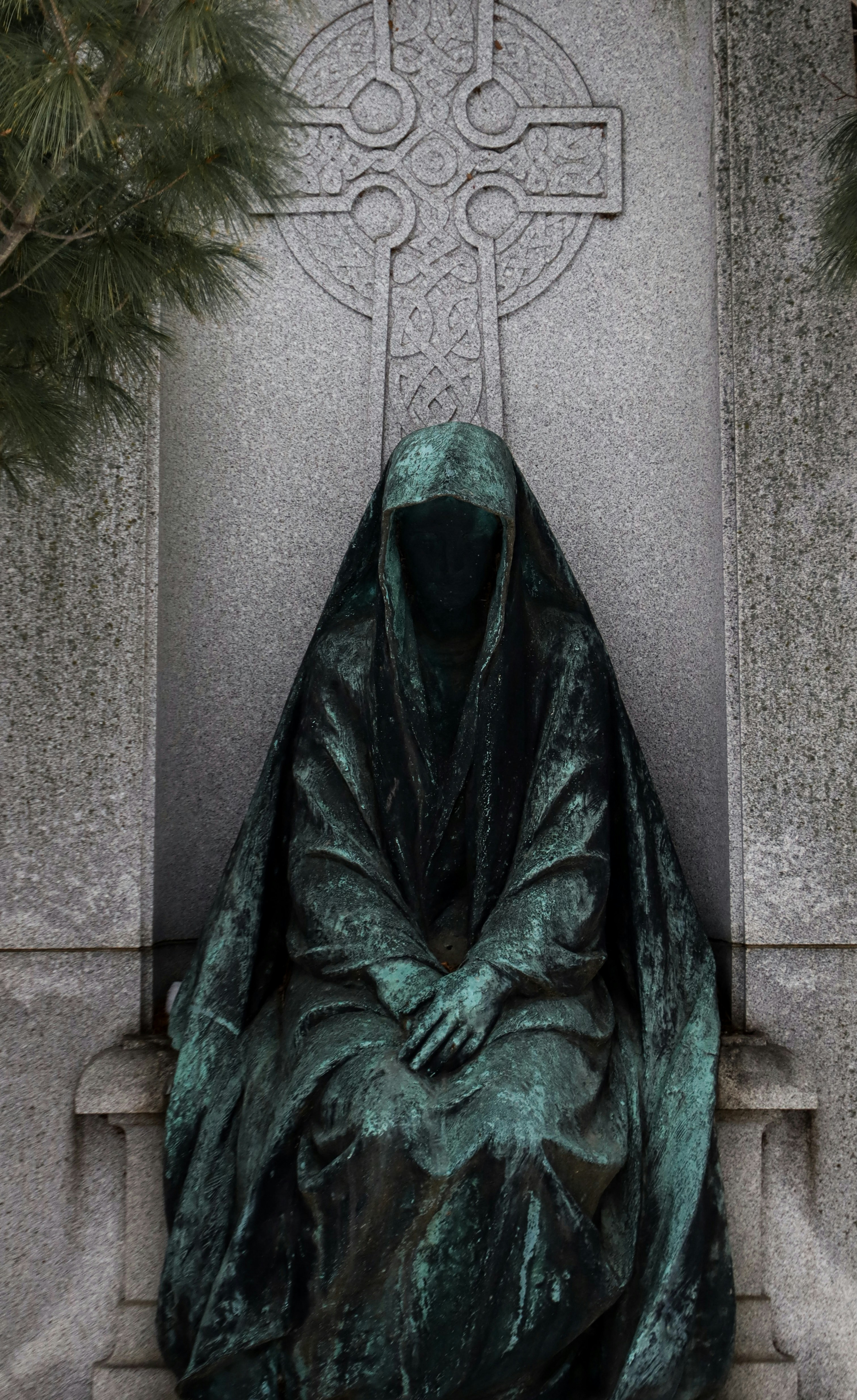 A cloaked statue sits before a celtic cross.