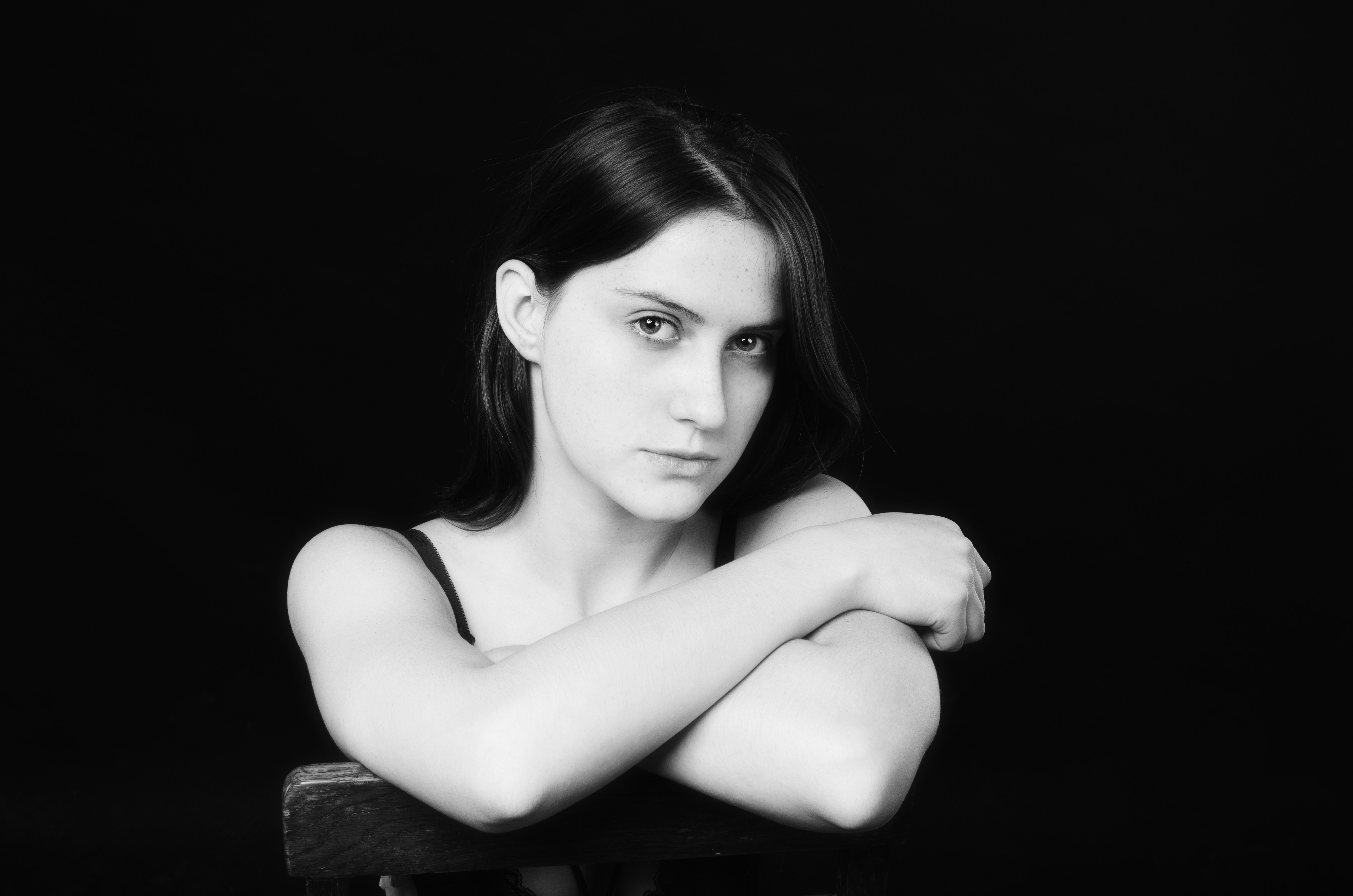 A young woman with dark hair sits with arms crossed.