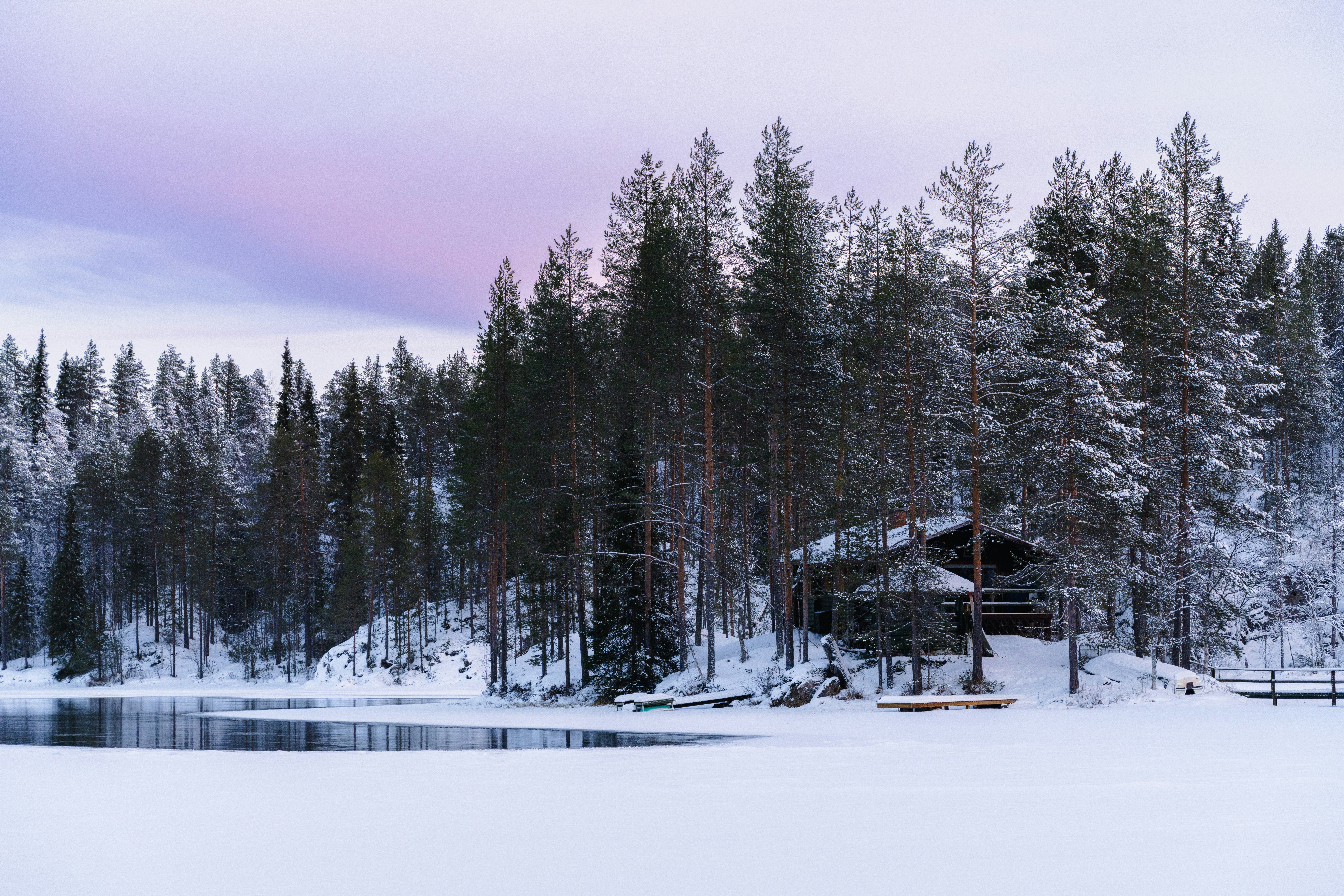Schneebedeckter Wald mit einer Hütte an einem zugefrorenen See