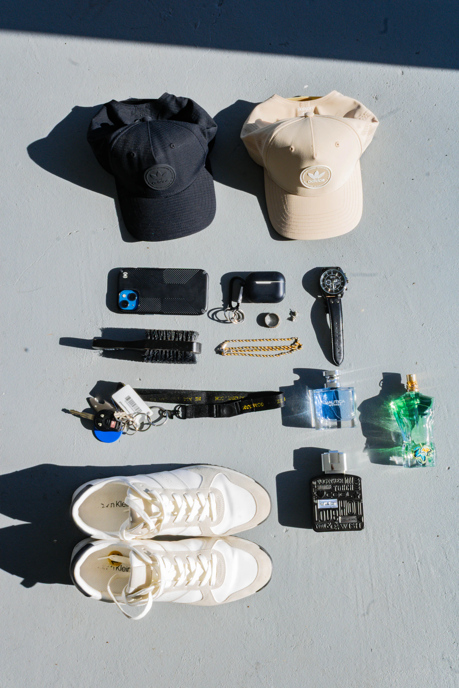Men's accessories laid out: caps, phone, cologne, sneakers
