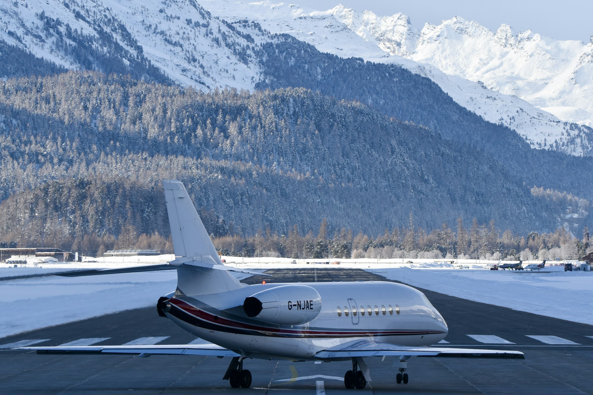 A business jet on a snowy runway below mountains