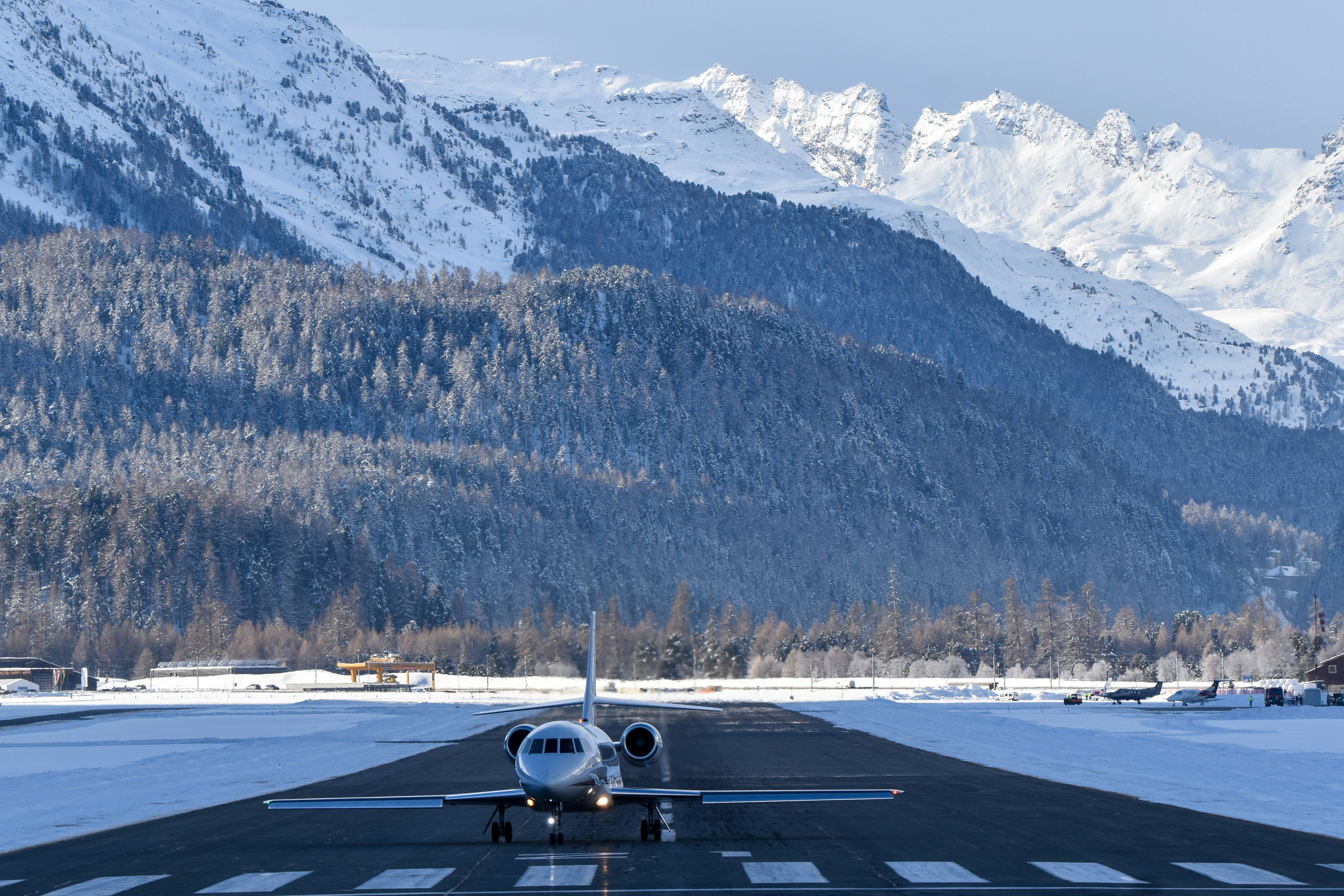 Un jet privado en una pista nevada con montañas detrás.