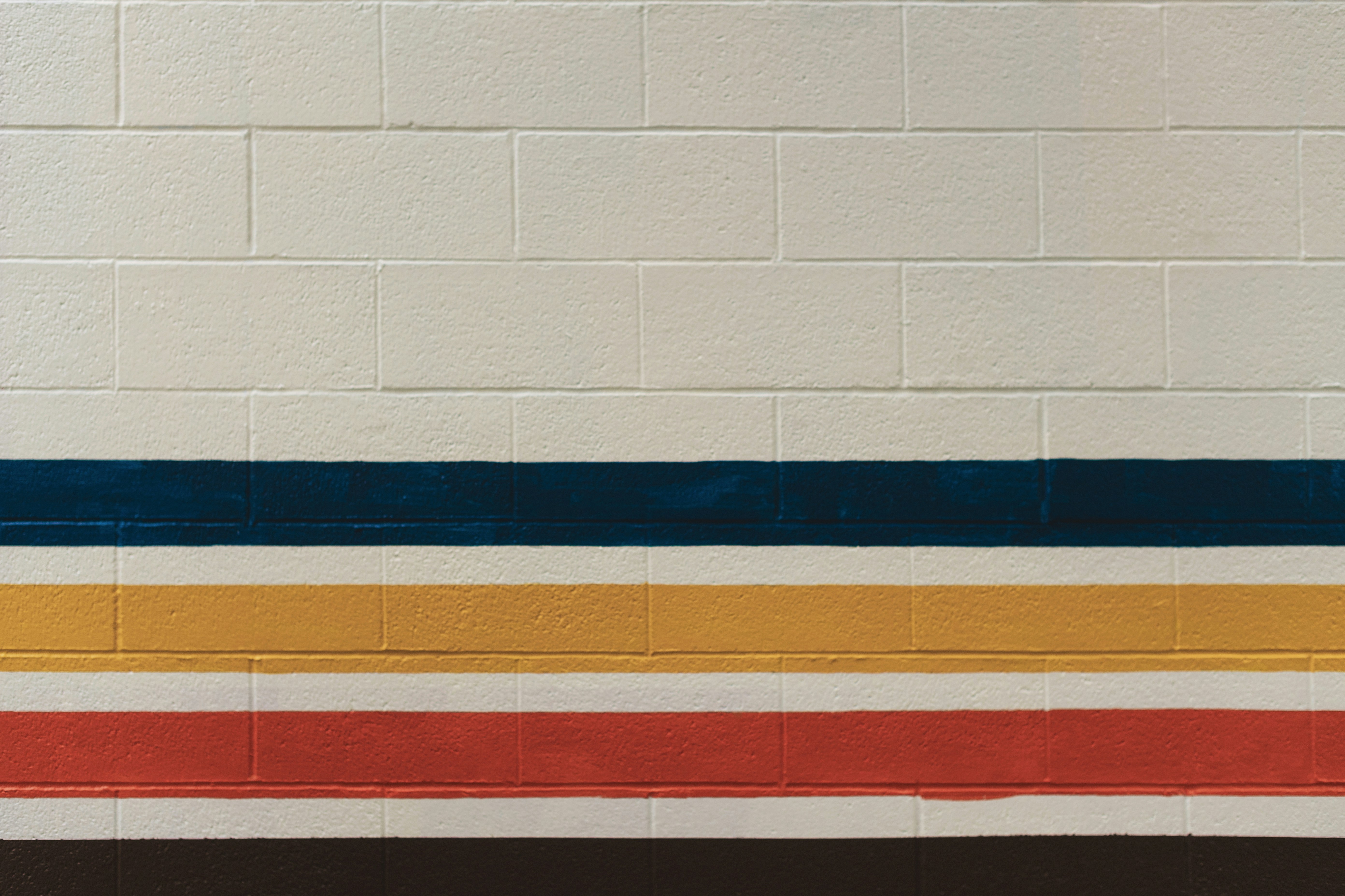 Photo of White brick wall with blue, yellow, and red stripes by Tim Mossholder