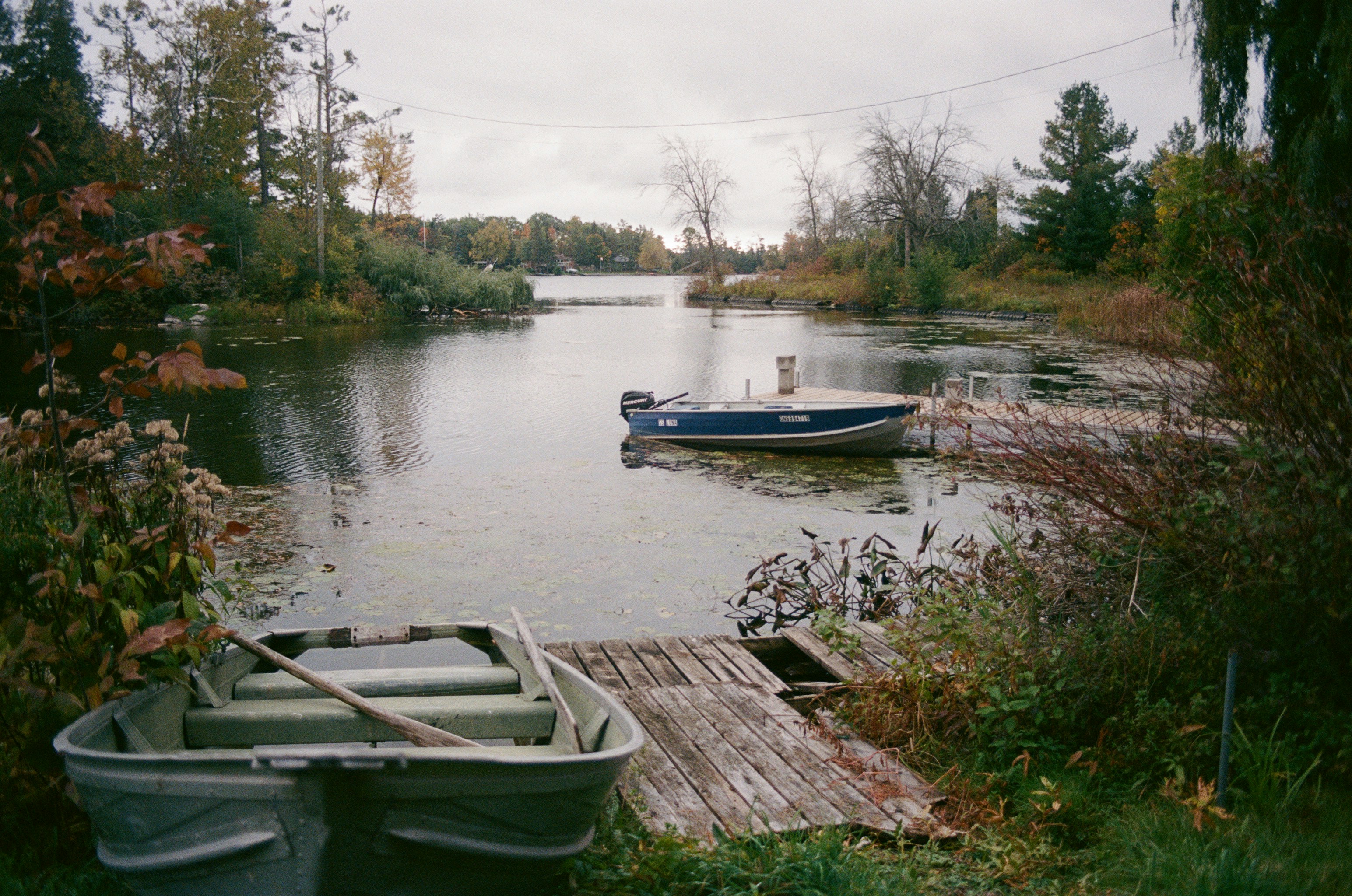 Two boats docked on a calm lake surrounded by trees.