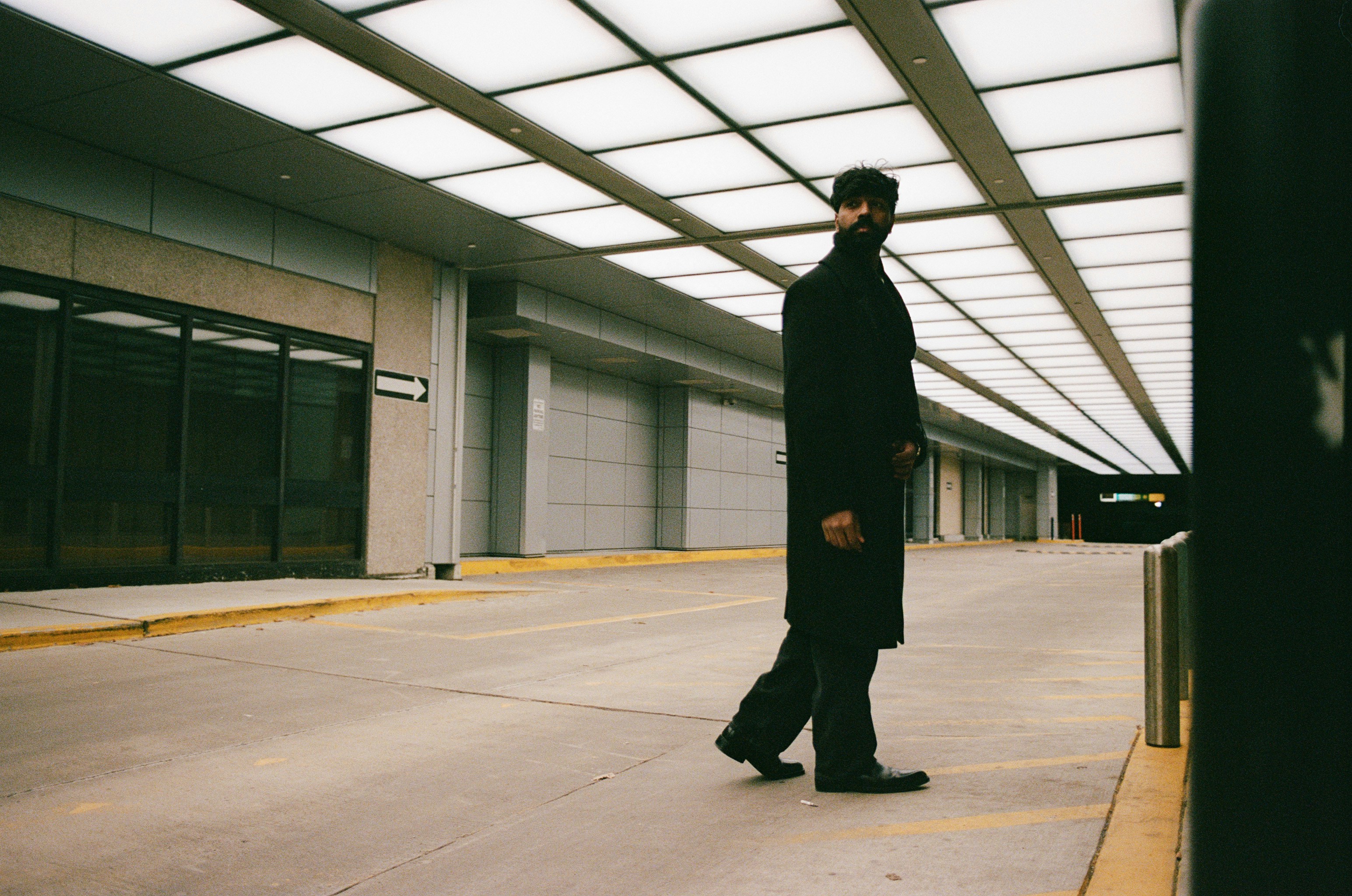 Man in dark coat walks down modern hallway
