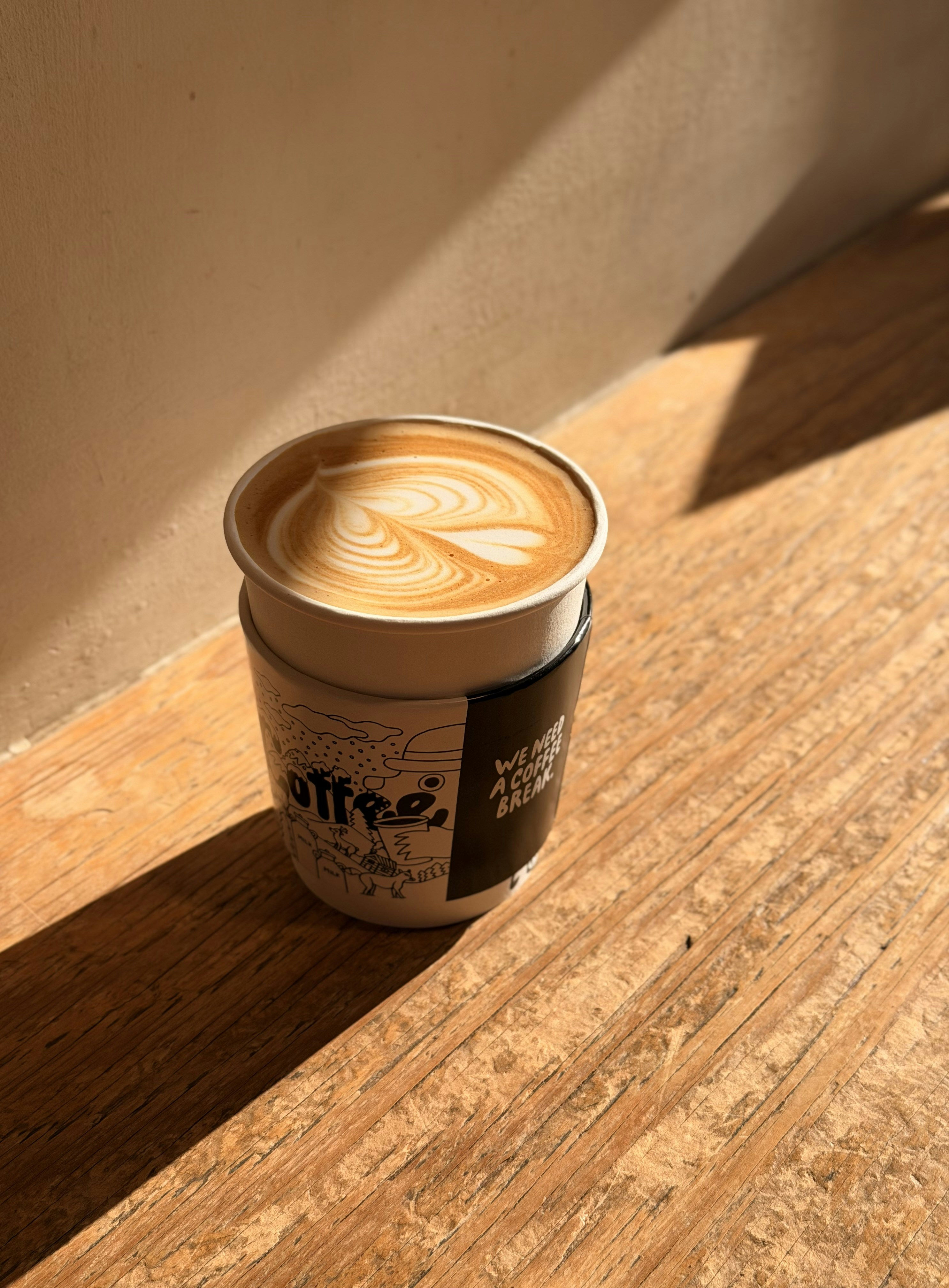 A latte with artfully poured foam sits on wood.