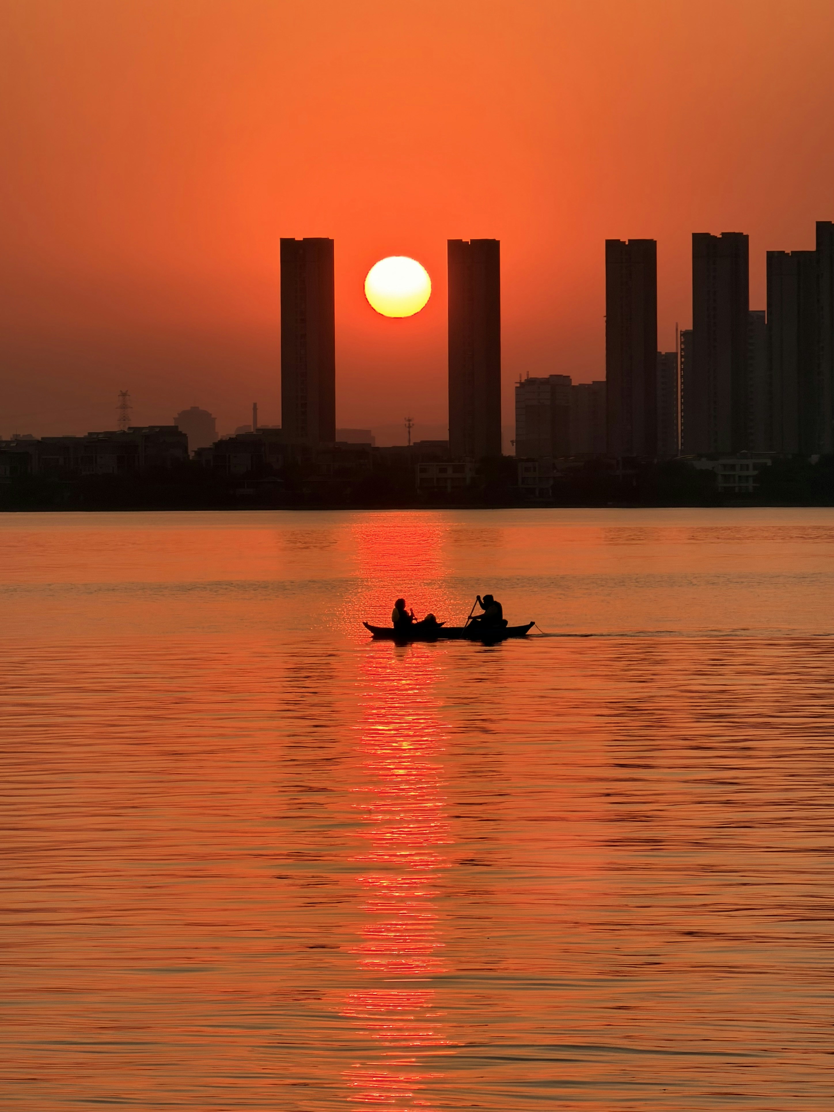Two people in a boat at sunset with city skyline