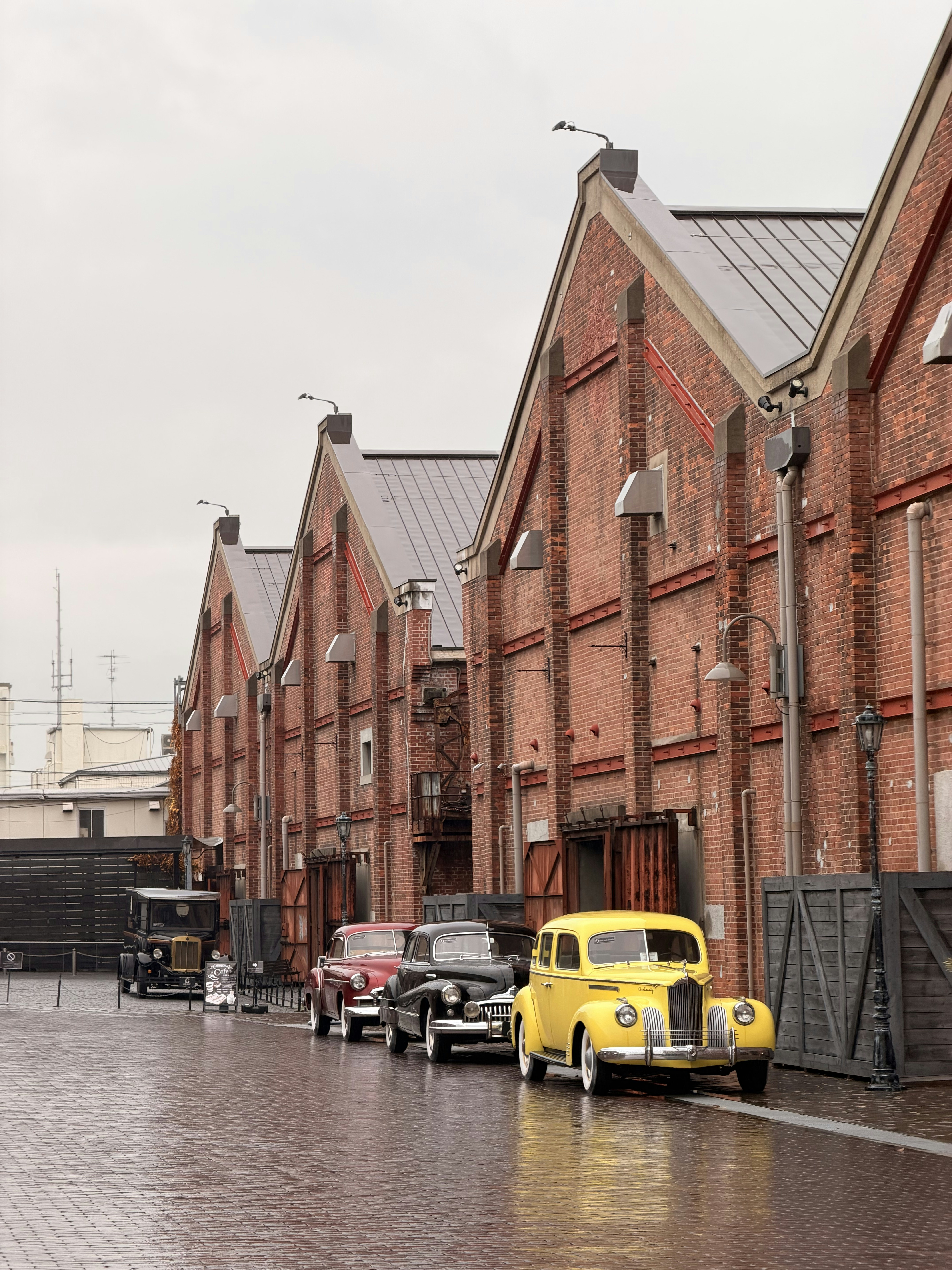 Vintage cars parked outside brick buildings on a wet day.