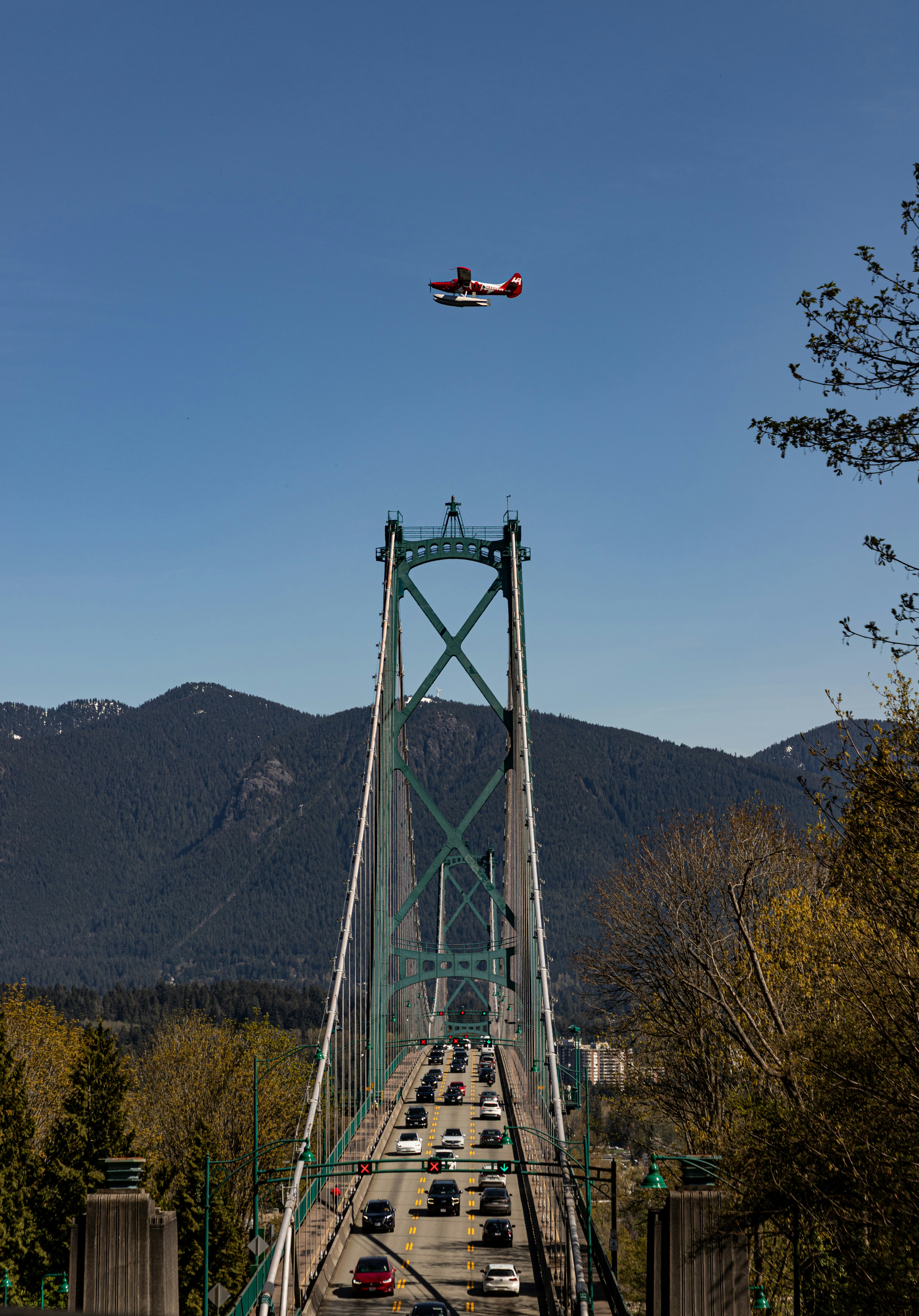 Seaplane flies over a busy bridge with mountains beyond.