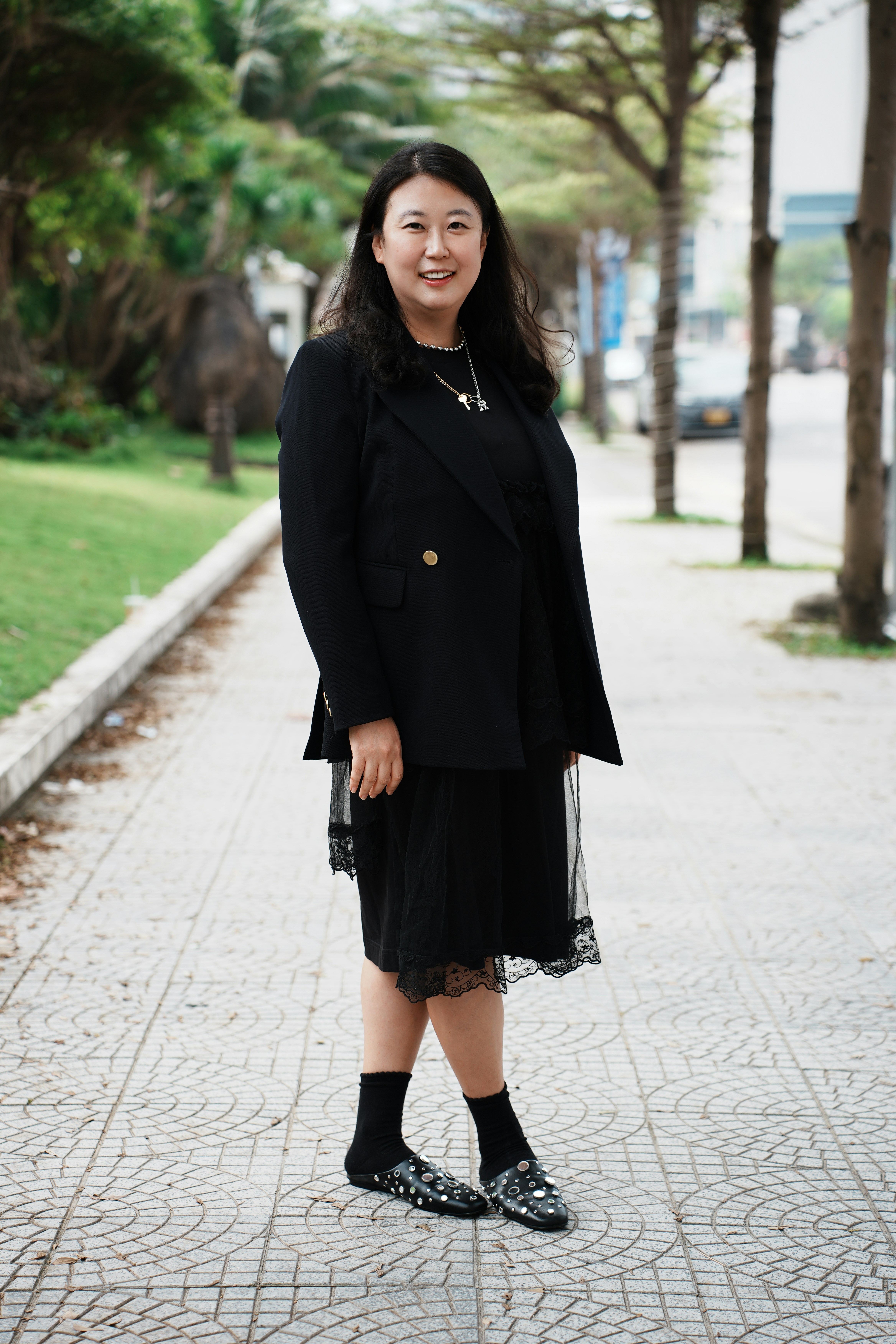 A woman in a black dress and blazer smiles.
