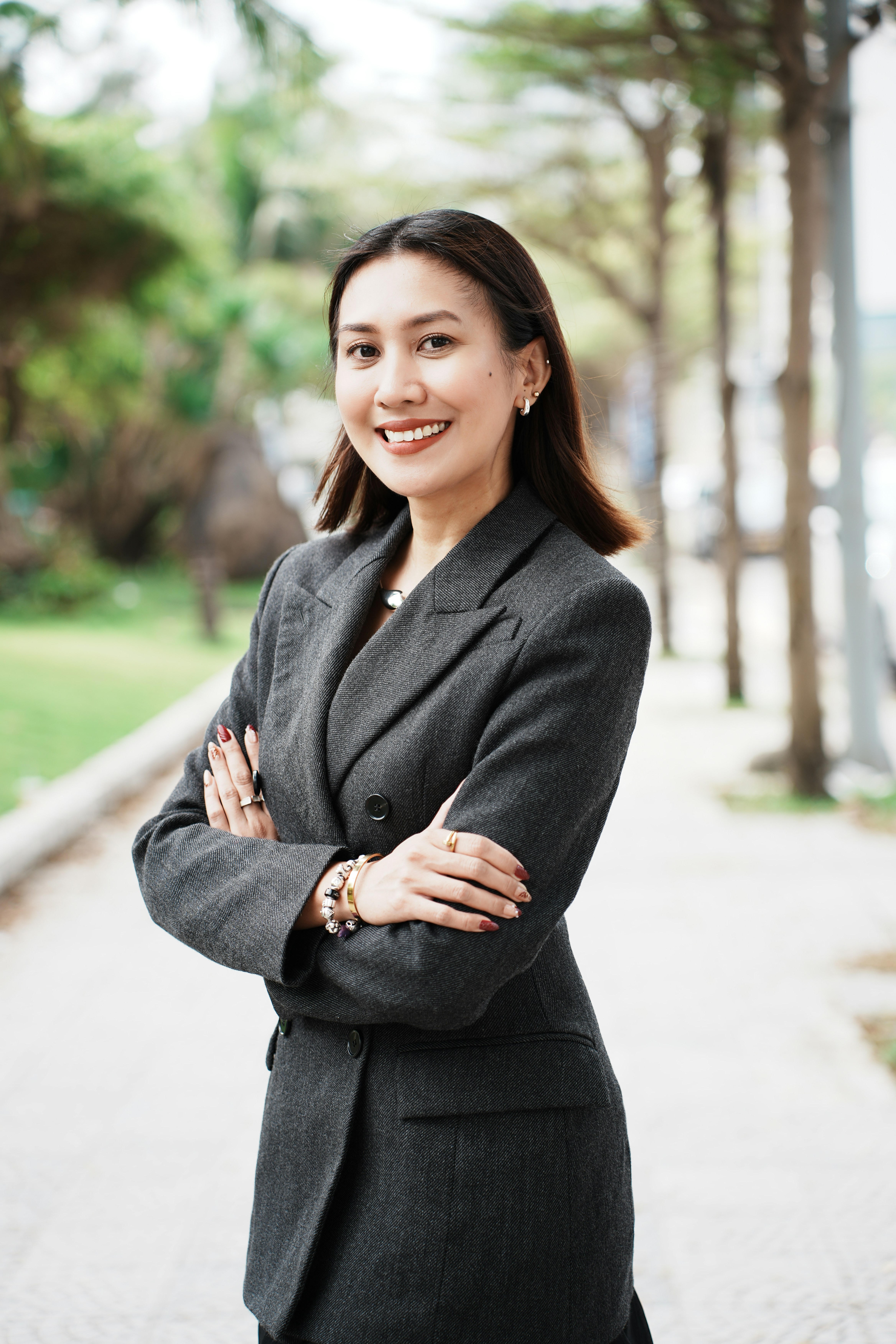 A smiling woman in a grey suit stands outdoors.