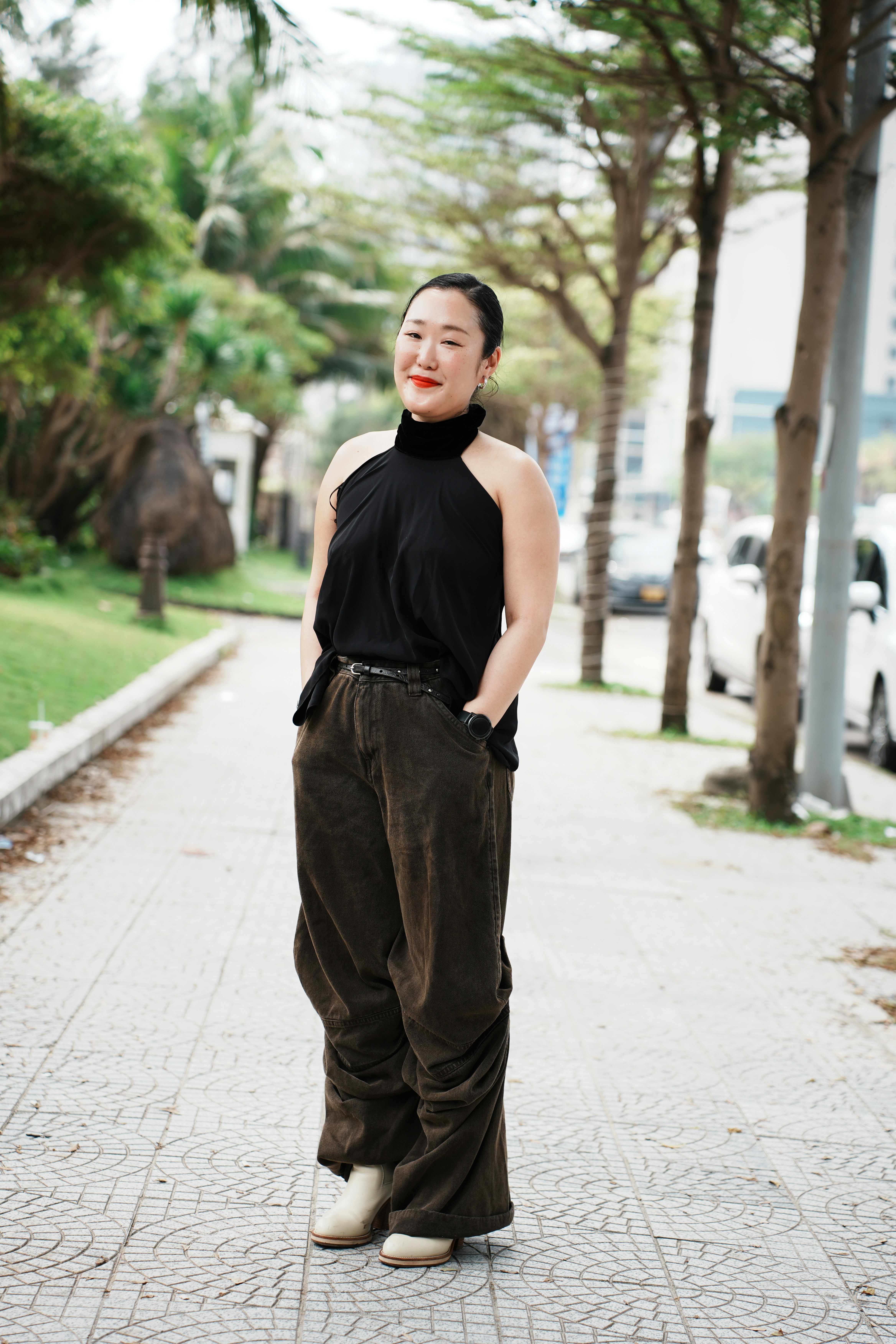 A woman stands on a paved sidewalk with trees.