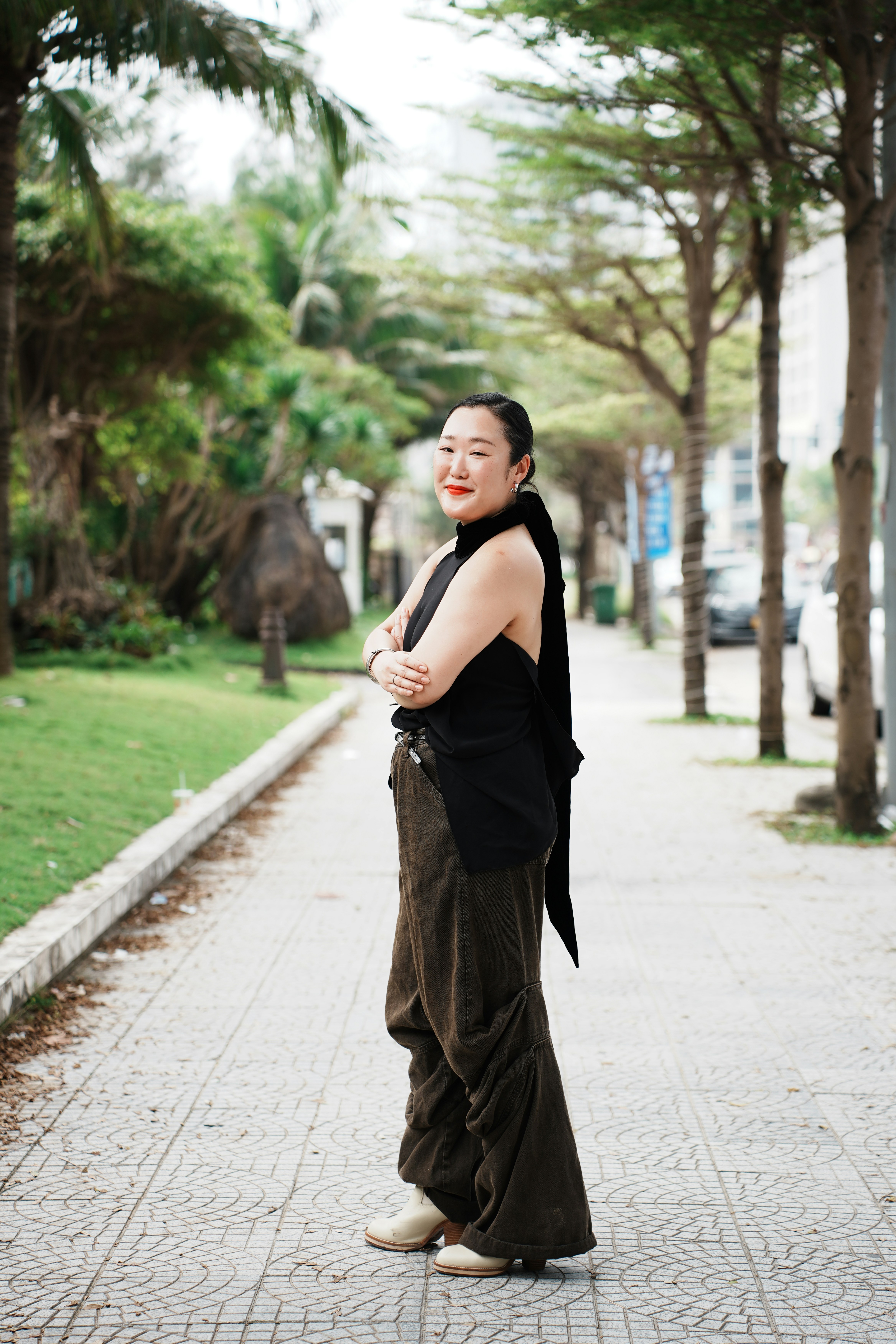 A woman in stylish clothing stands on a paved walkway.