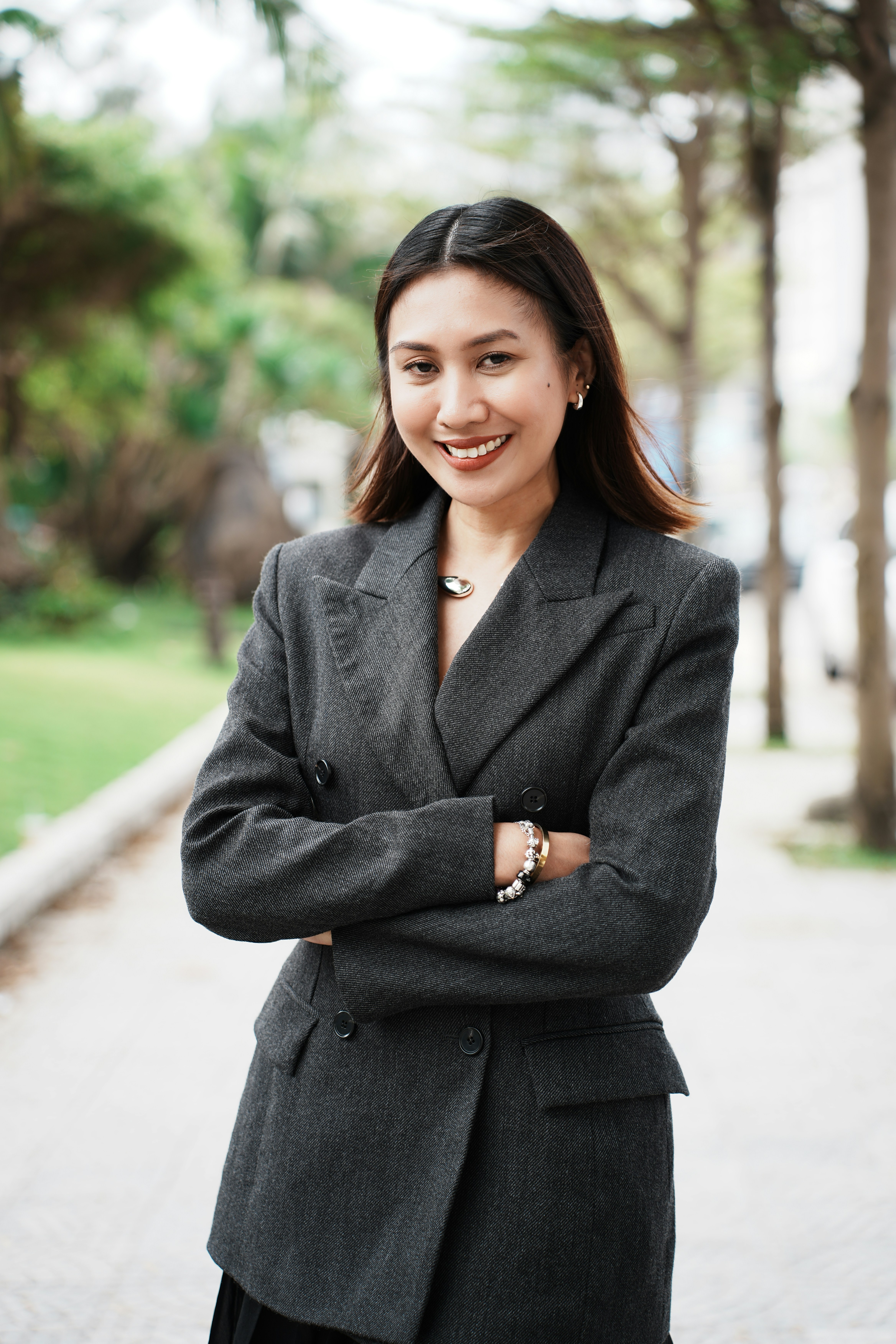 A woman in a grey blazer smiles with arms crossed.