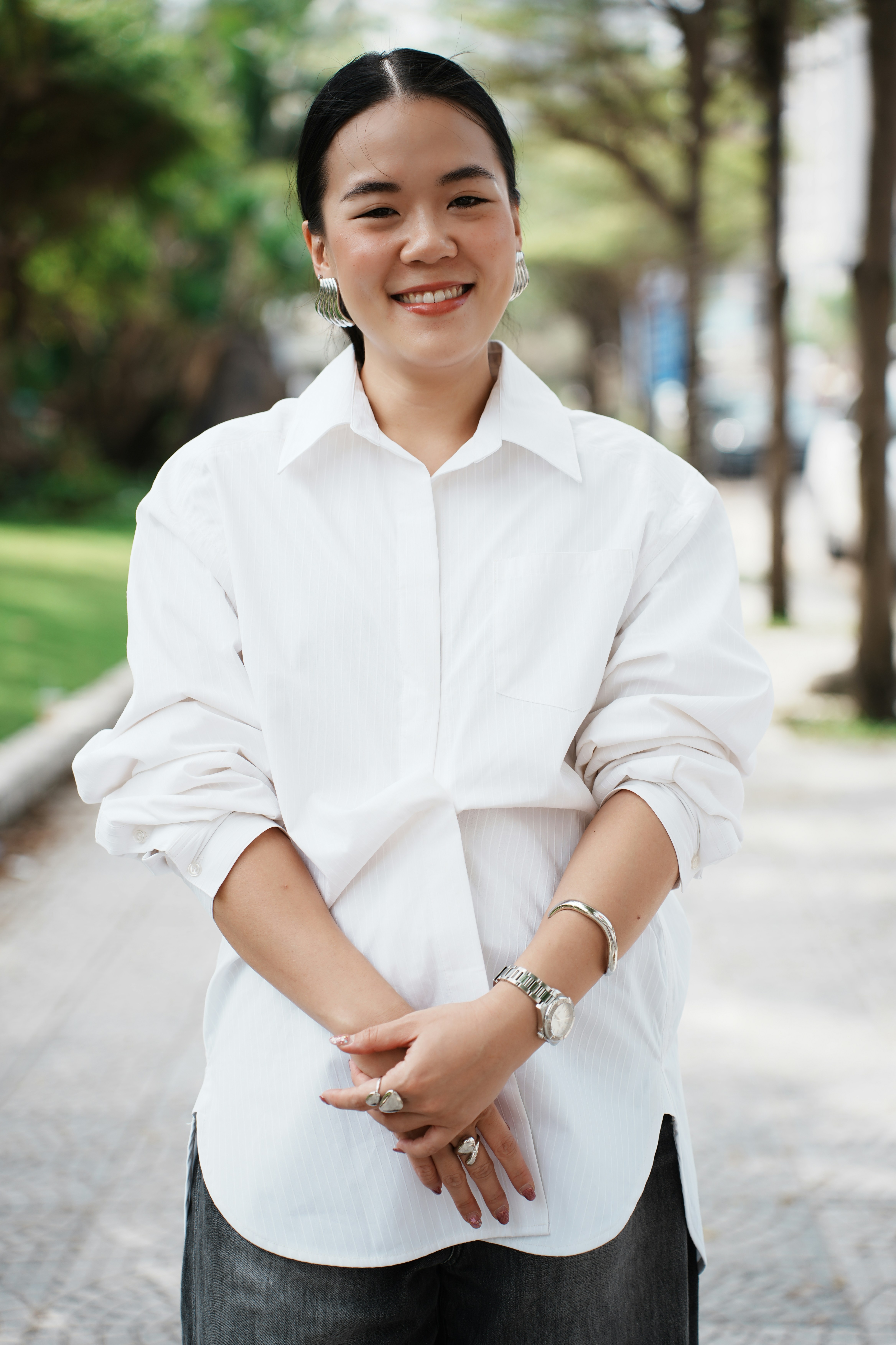 A young woman in a white shirt smiles outdoors.