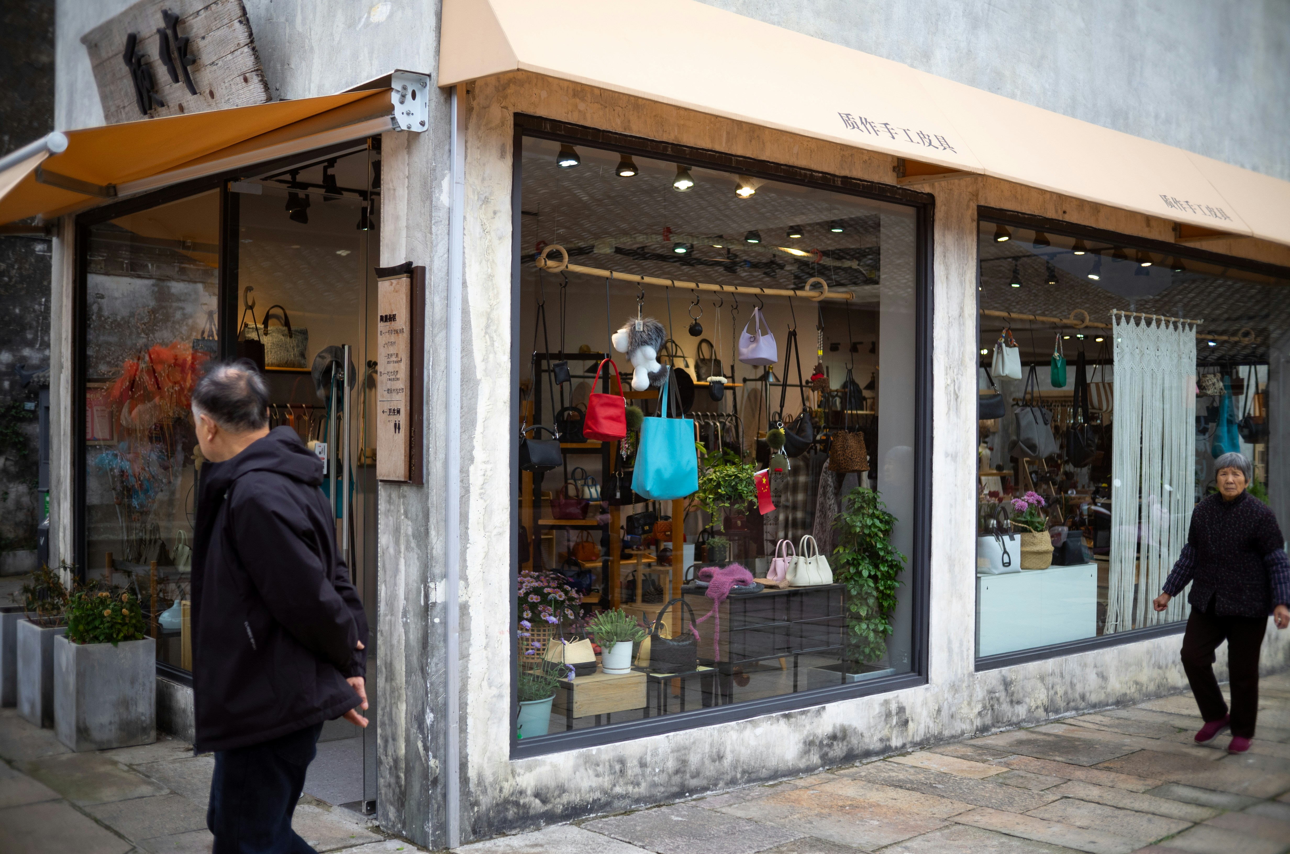 People walk past a boutique store with colorful bags displayed.