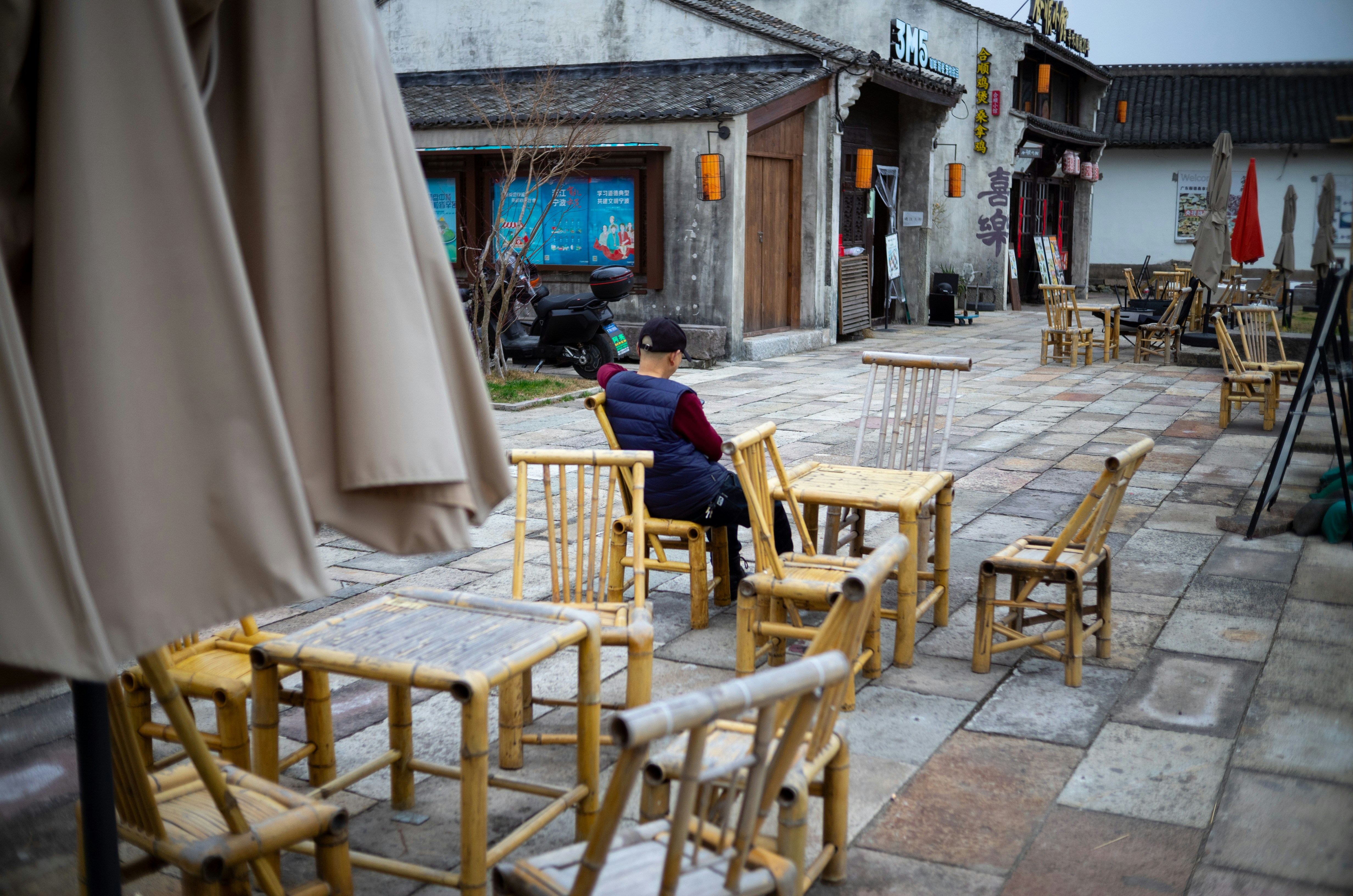 Person sitting at outdoor cafe tables and bamboo furniture.