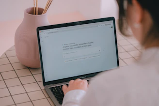 Woman typing on a laptop with a vase nearby