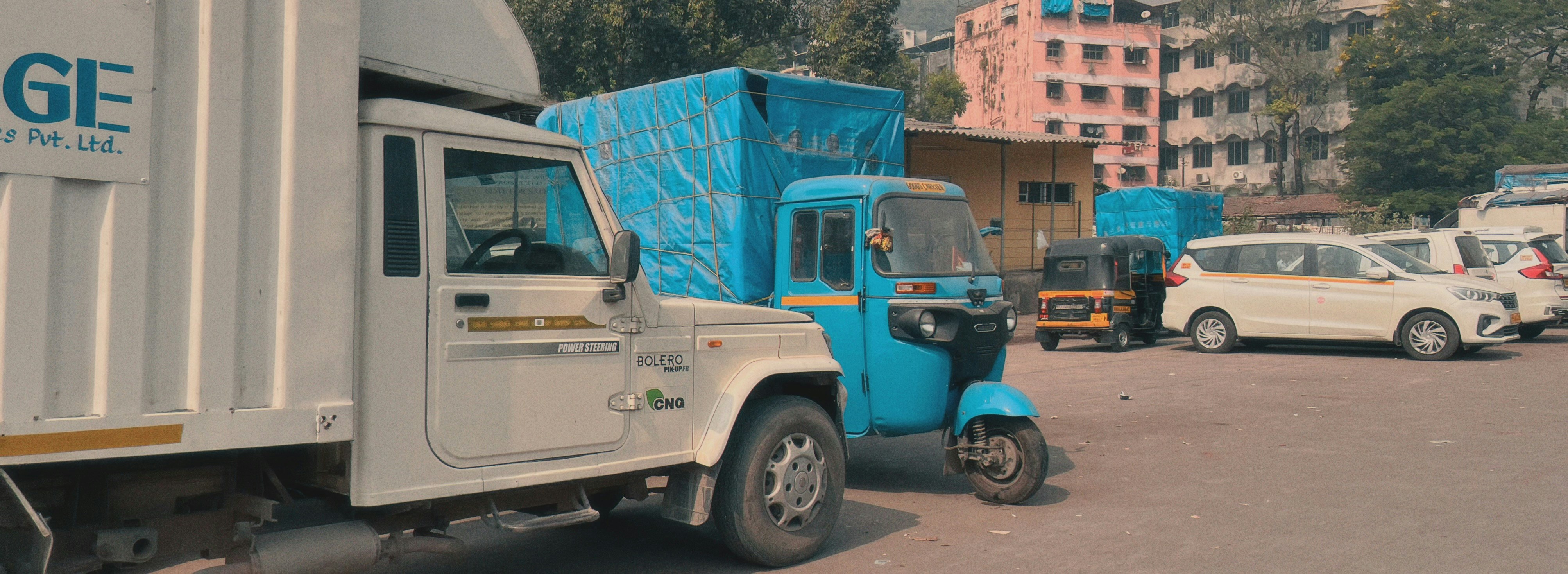 White truck, blue auto-rickshaw, and white car parked.