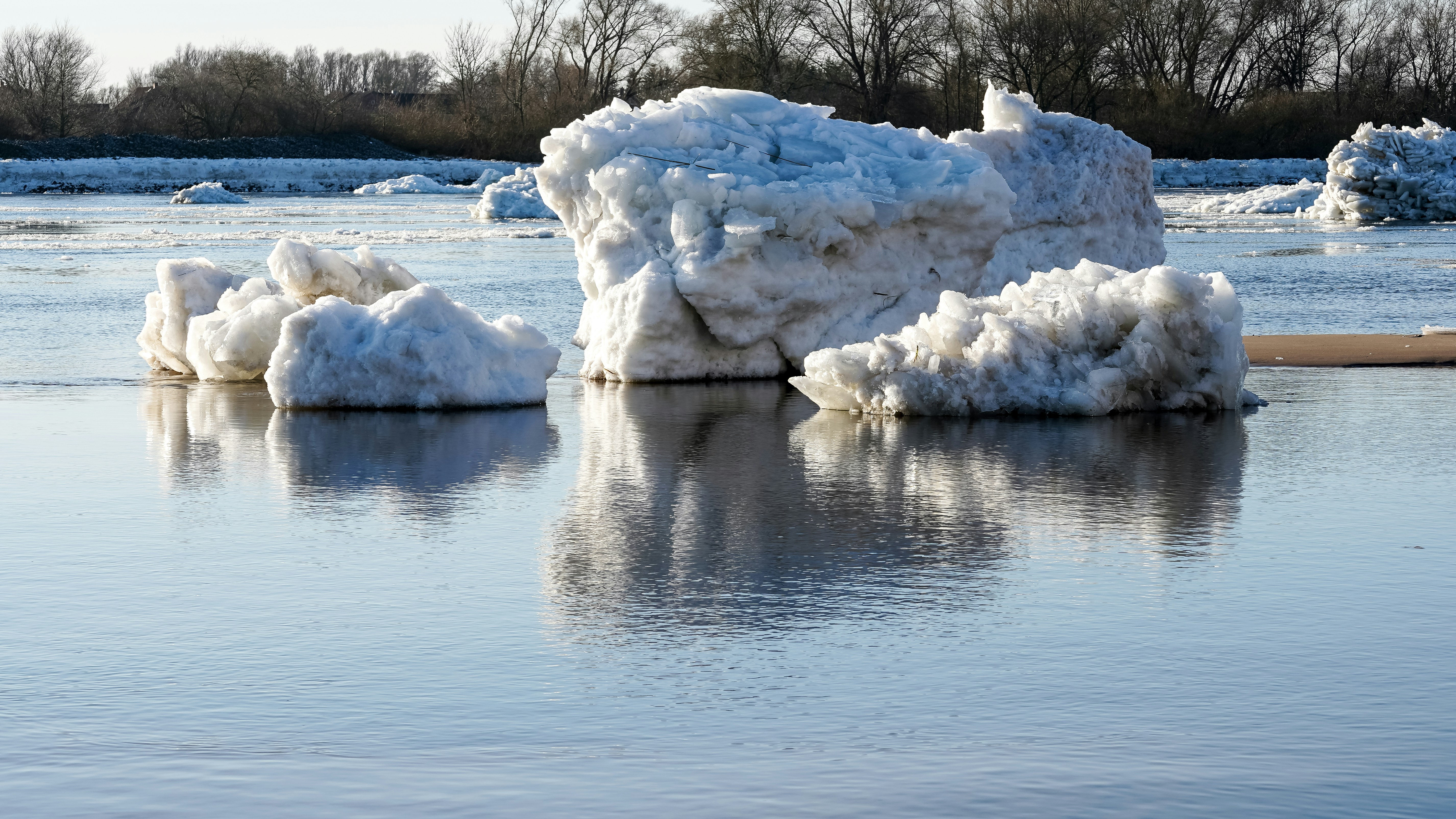Large ice chunks float on calm water with reflections