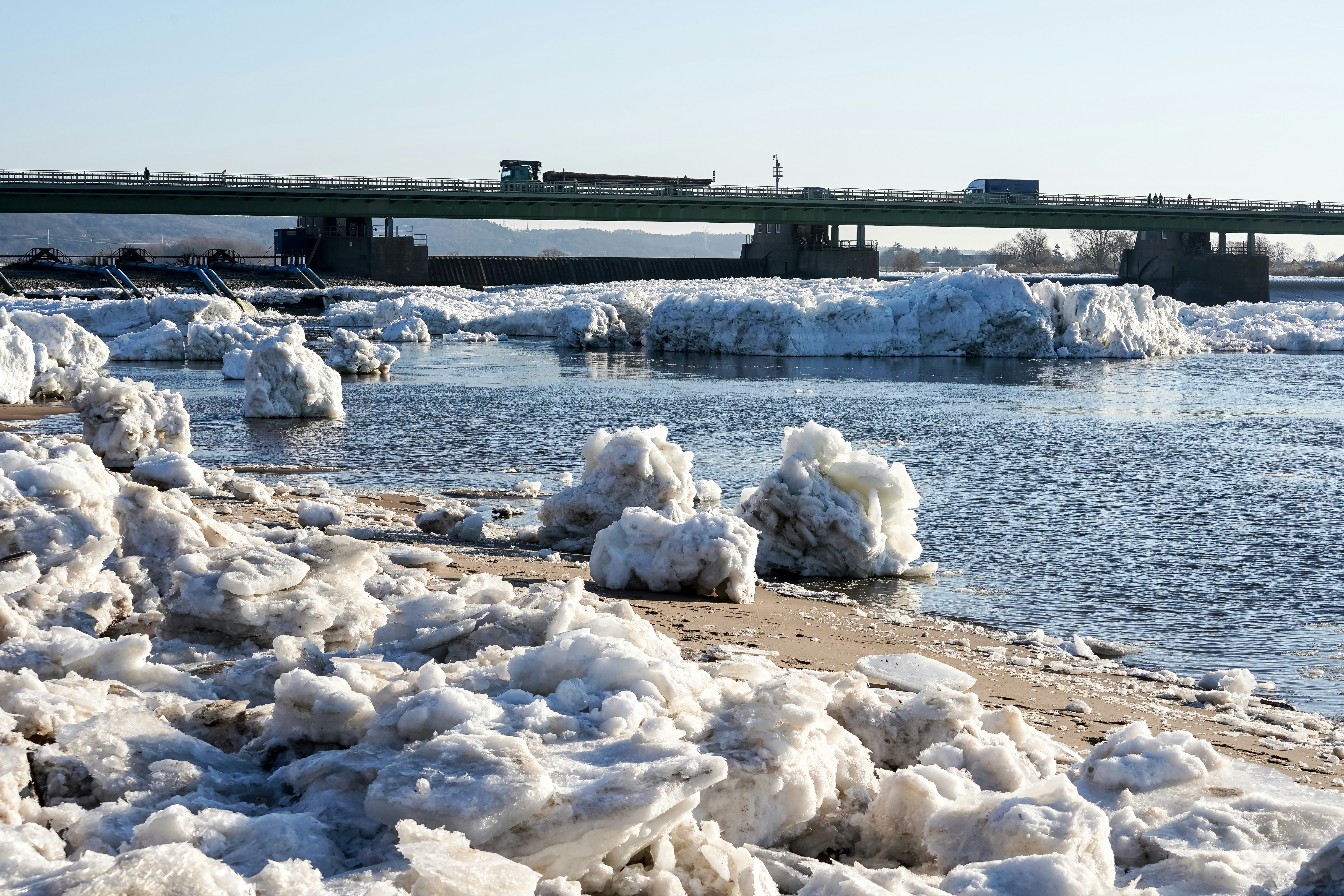 Ice chunks on a riverbank with a bridge in background