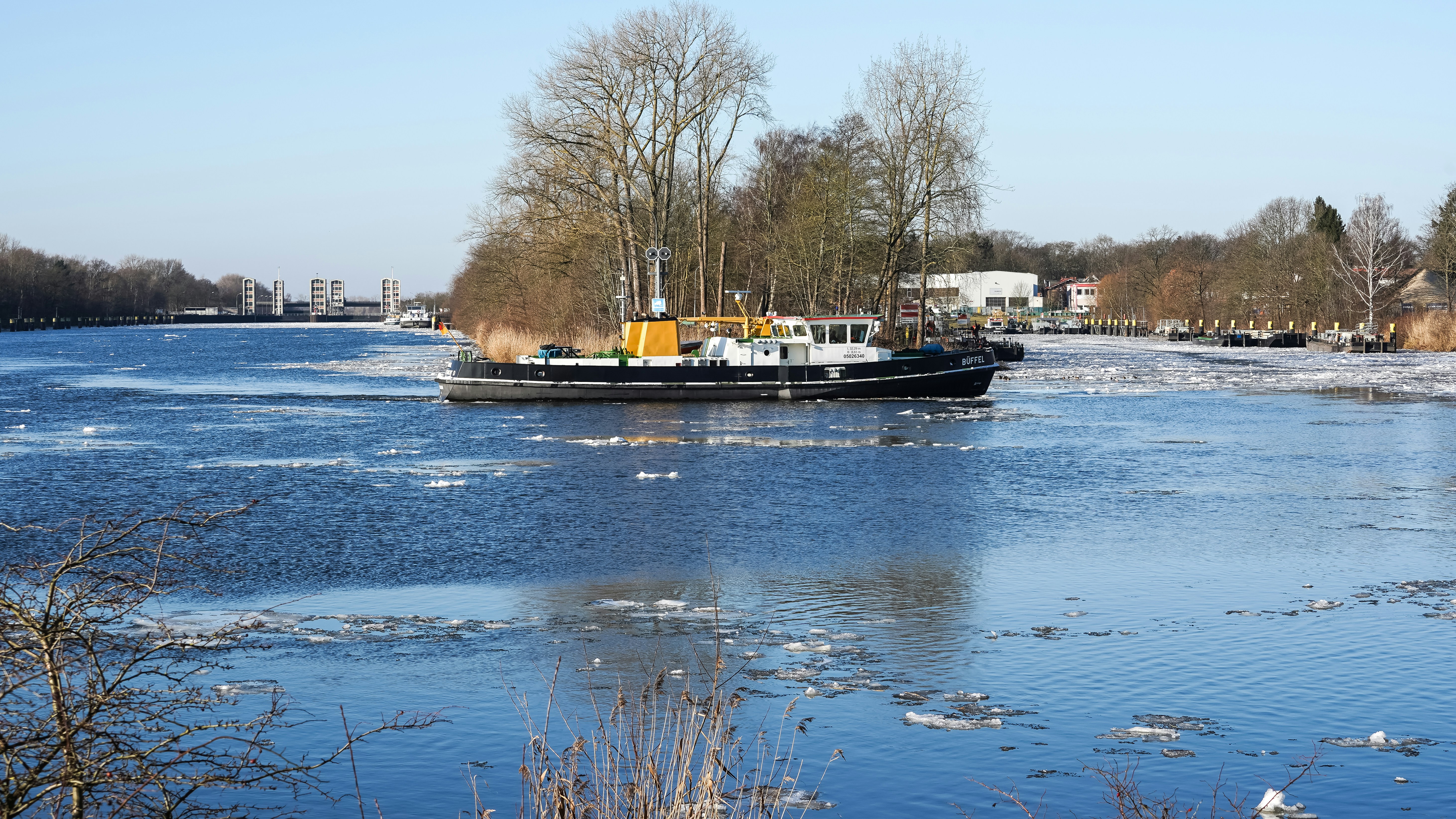 A boat navigates a partially frozen river with trees.