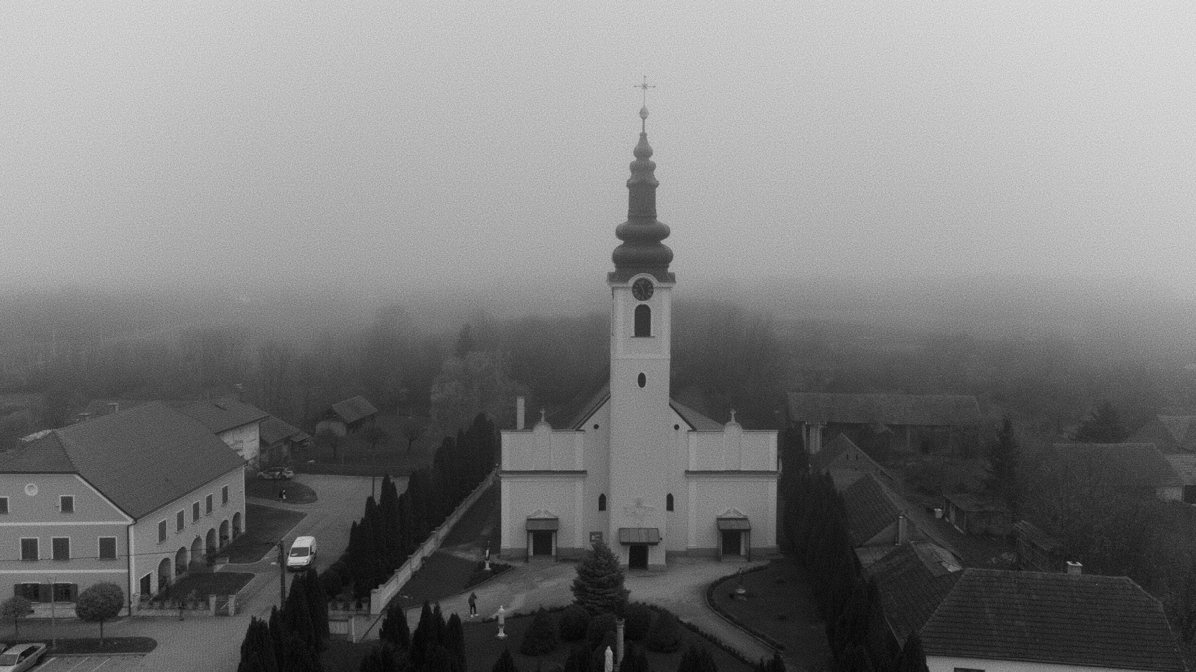 A white church steeple rises above a foggy village.