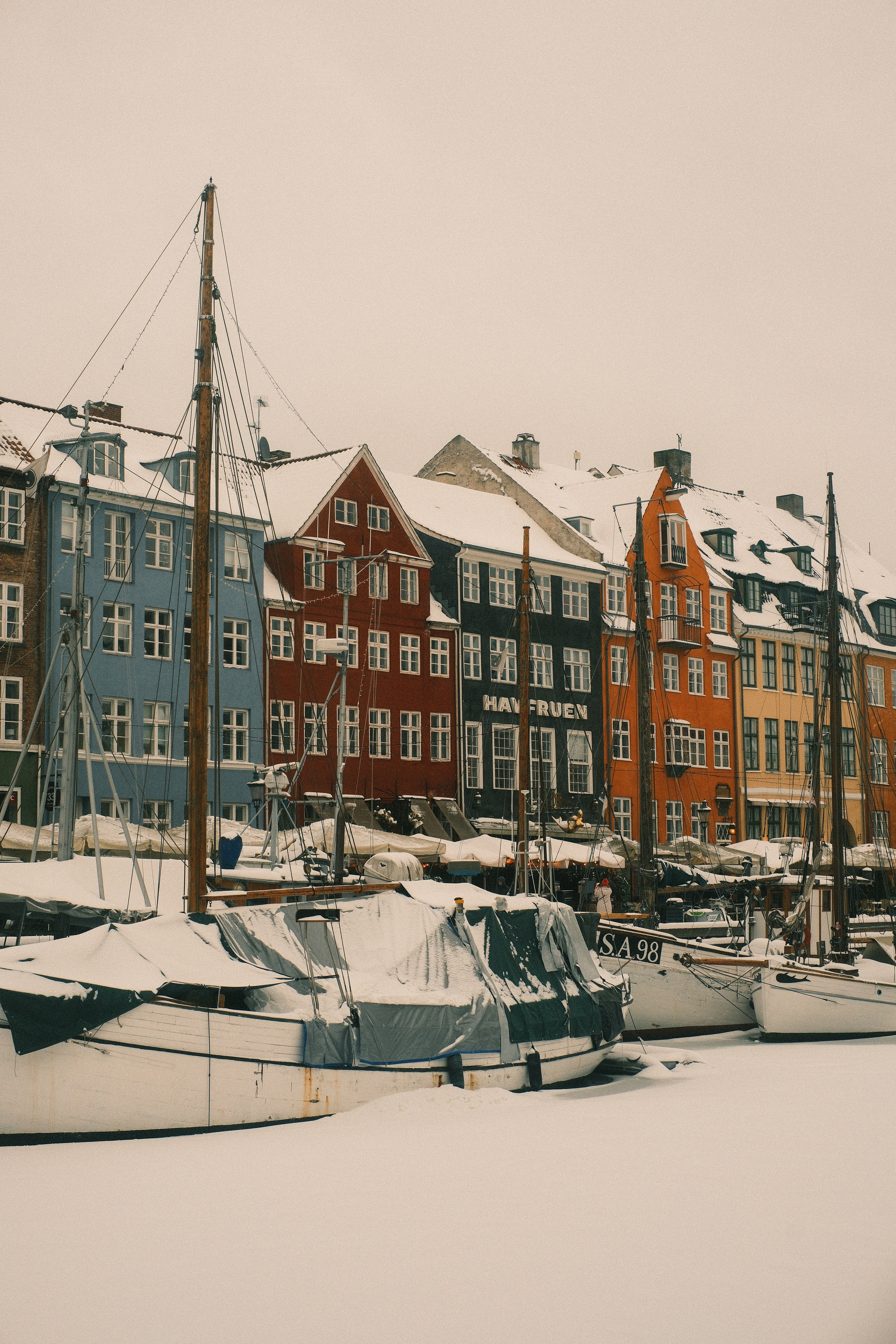 Colorful buildings line a snowy canal with boats.