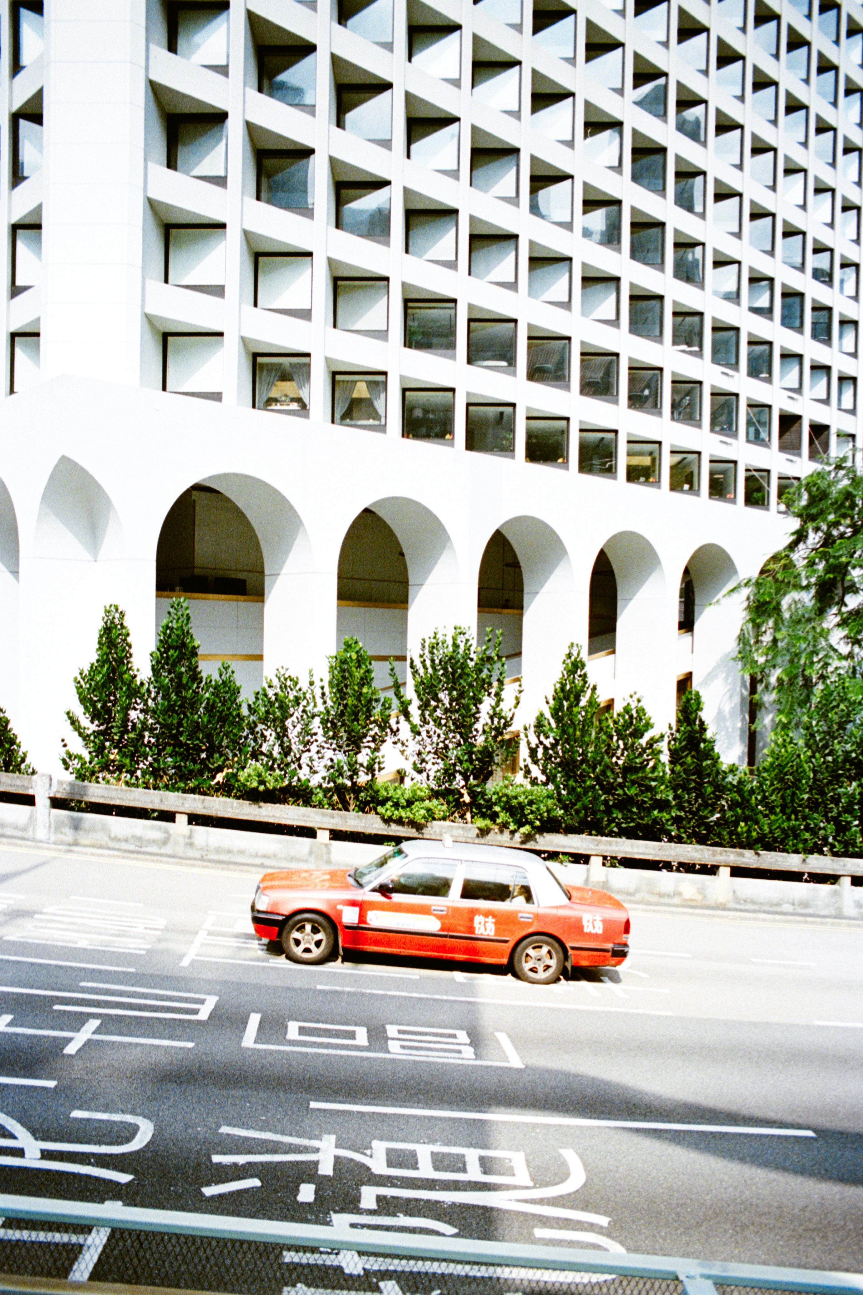 Red and white taxi drives past modern building arches.